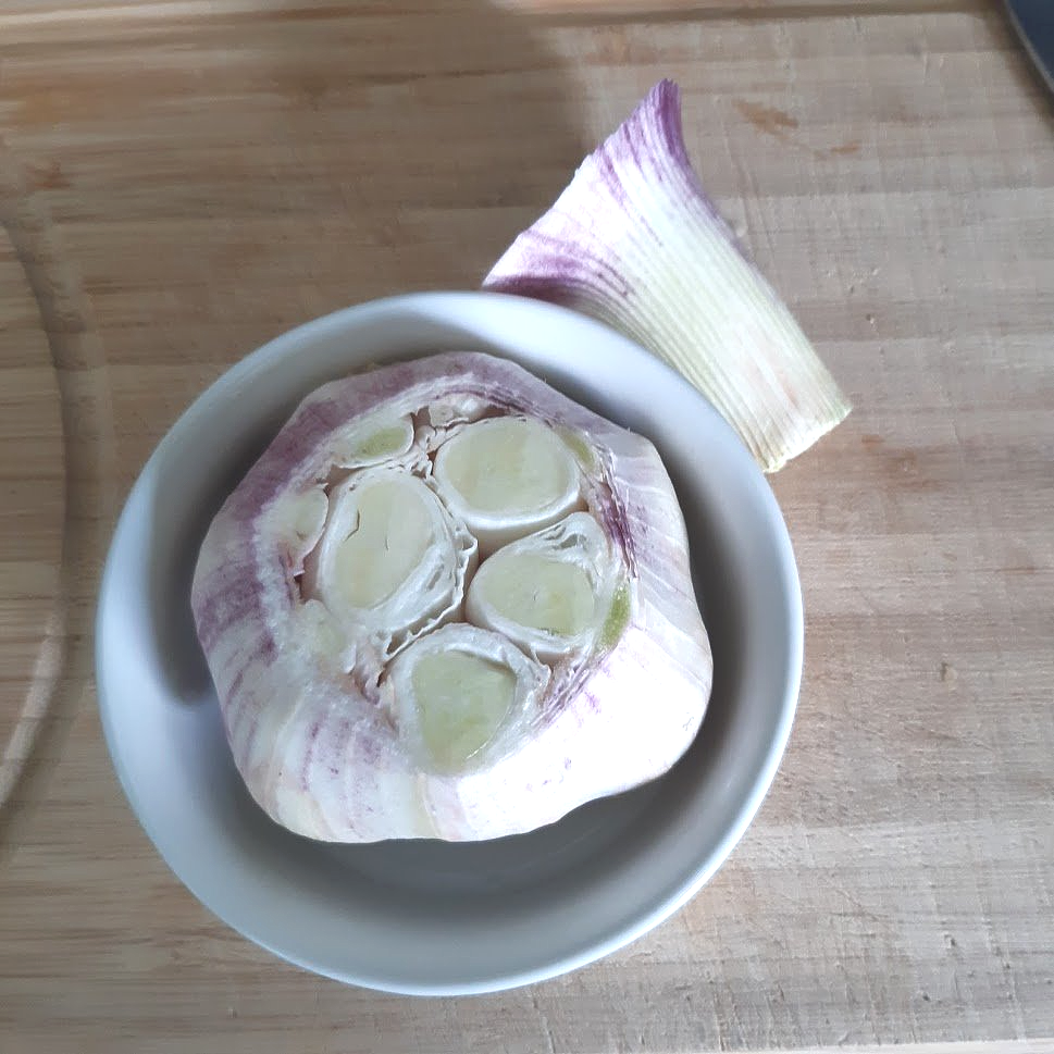 Een doormidden gesneden knoflookbol in een witte kom, op een houten ondergrond.