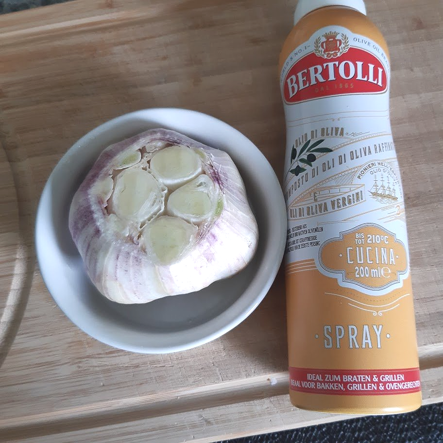Leg een bol knoflook in een kom en besprenkel een houten snijplank met olijfolie.