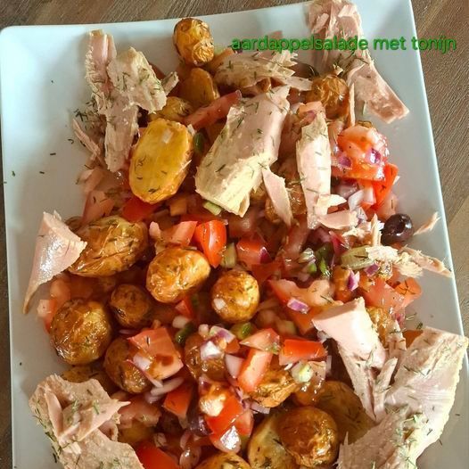 Aardappelsalade met tonijn, tomaten en olijven op een wit bord.