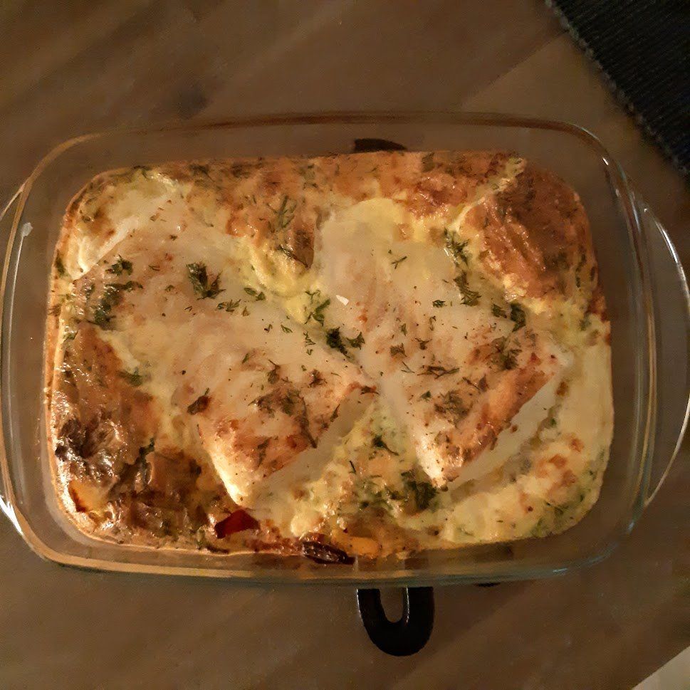Een ovenschotel met kip in een doorzichtige glazen ovenschaal. De kip is bedekt met luchtige eiwitten, kruiden en specerijen.