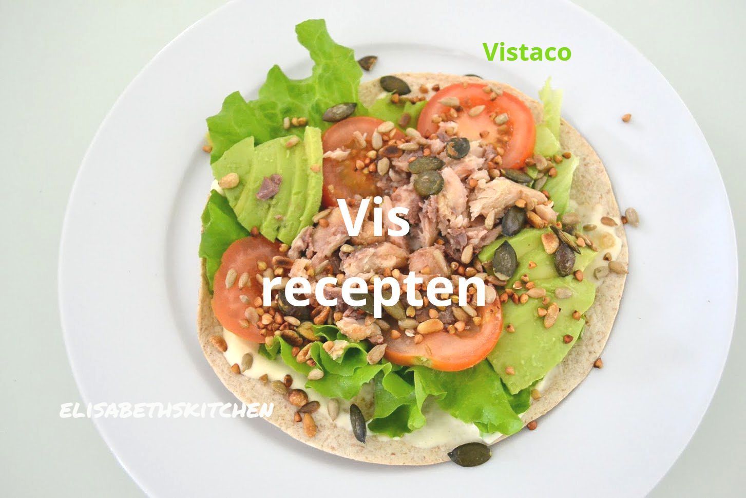 Vis taco op een wit bord met sla, avocado, tomaat en zaden.