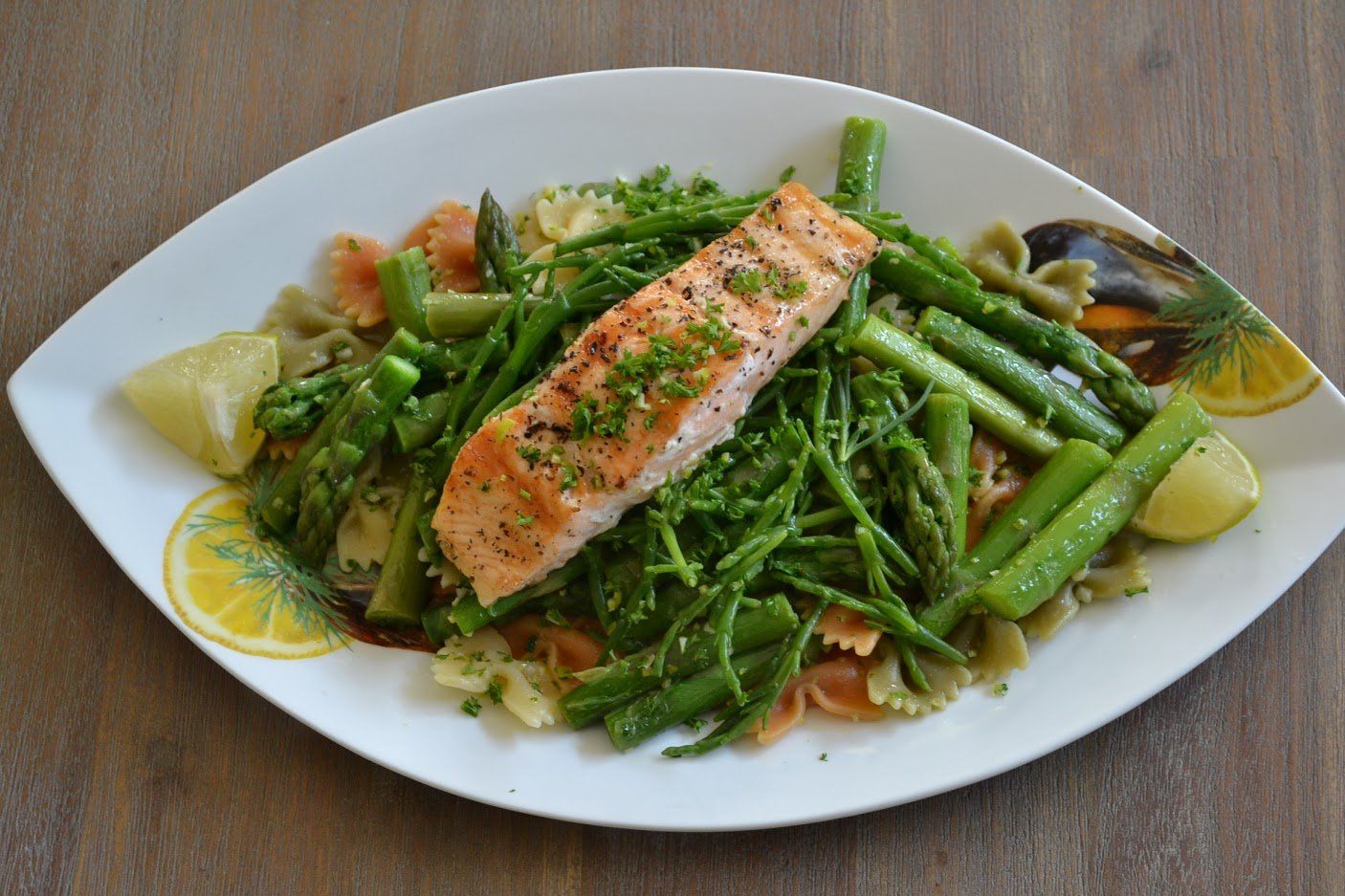 Zalmfilet met asperges en pasta op een wit bord, gegarneerd met citroen.