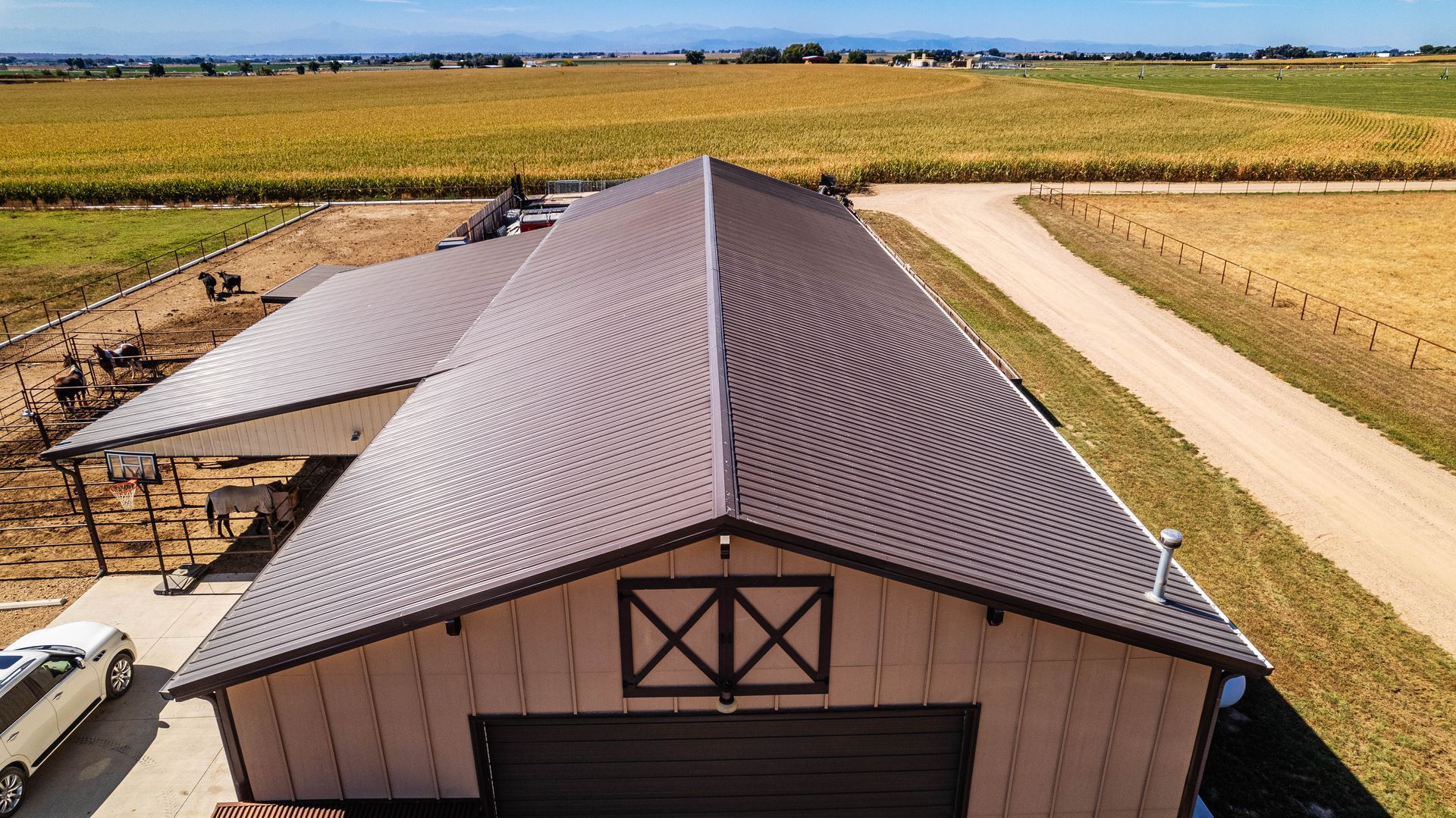 Brown metal roof on tan barn in a rural setting, with a white car parked nearby.