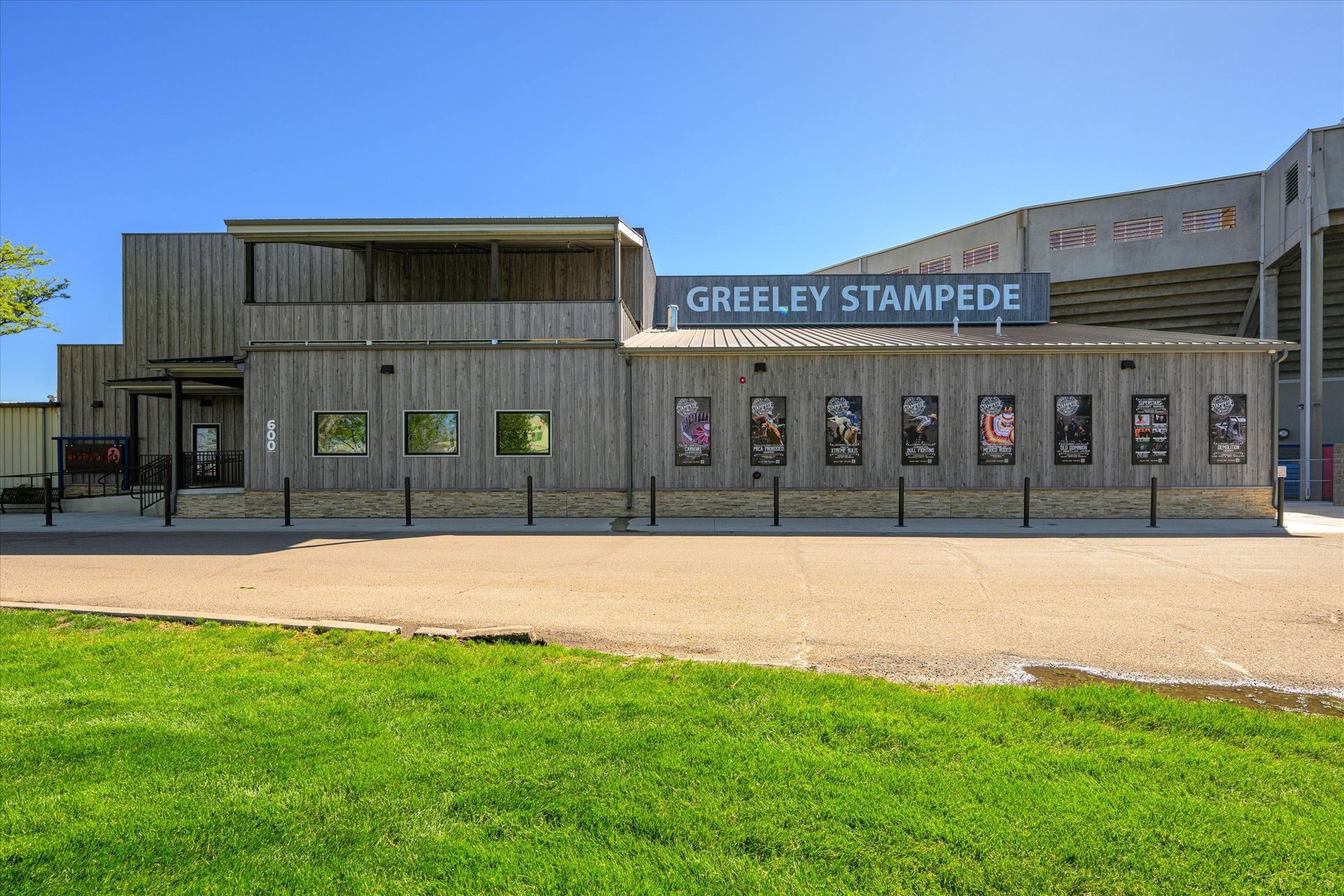 Greeley Stampede building with posters, a wooden facade, and a stadium in the background under a blue sky.