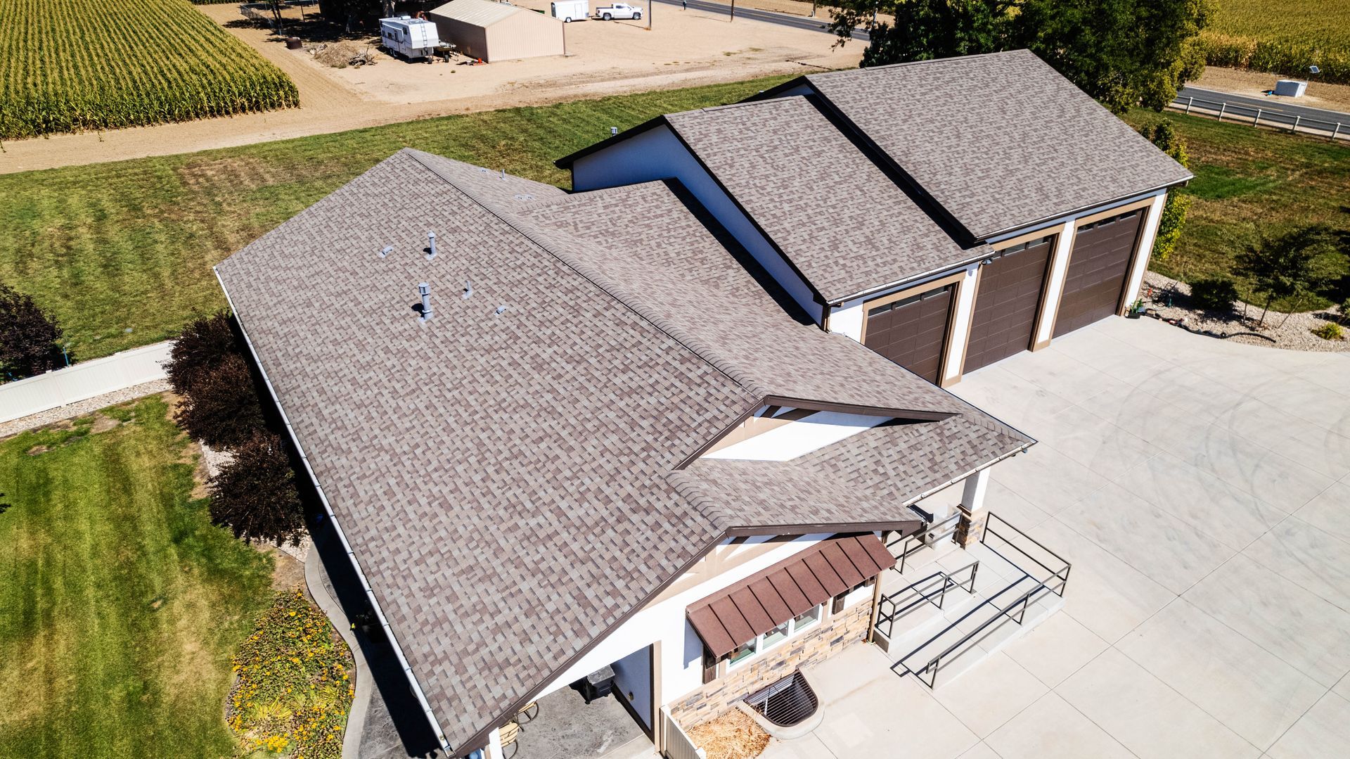 Aerial view of a white building with a brown shingled roof, three garage doors, and a concrete driveway.
