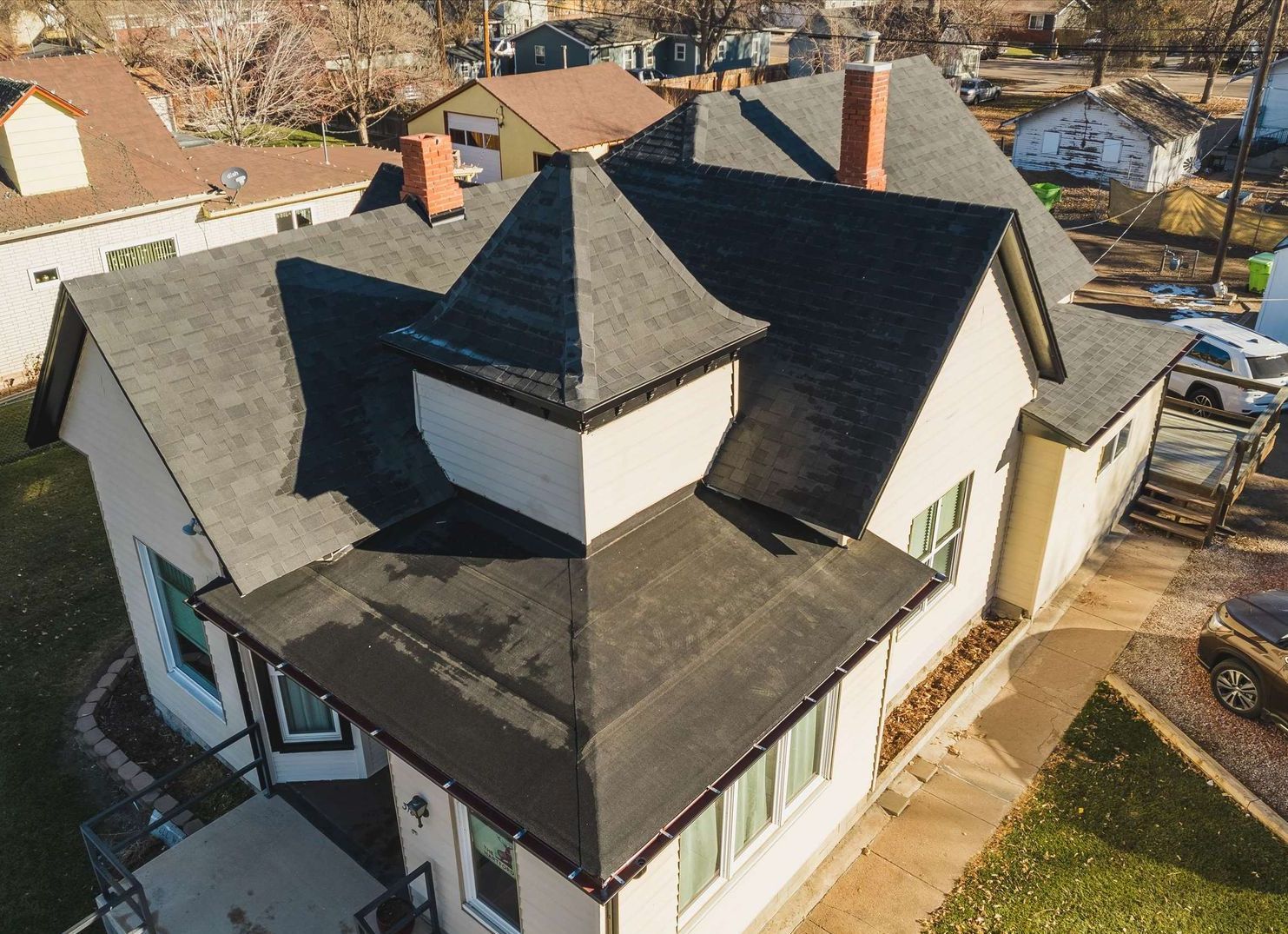 Aerial view of a two-story house with dark gray roof, light beige siding, and brown trim.