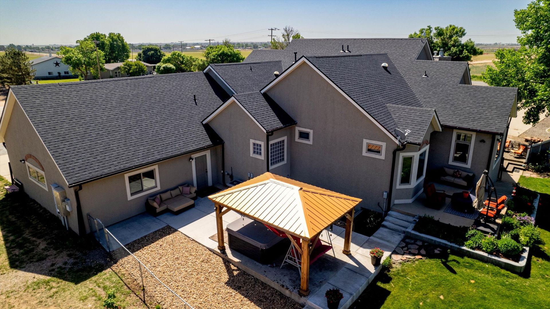 Gray house with black roof, gazebo, and yard on a sunny day.