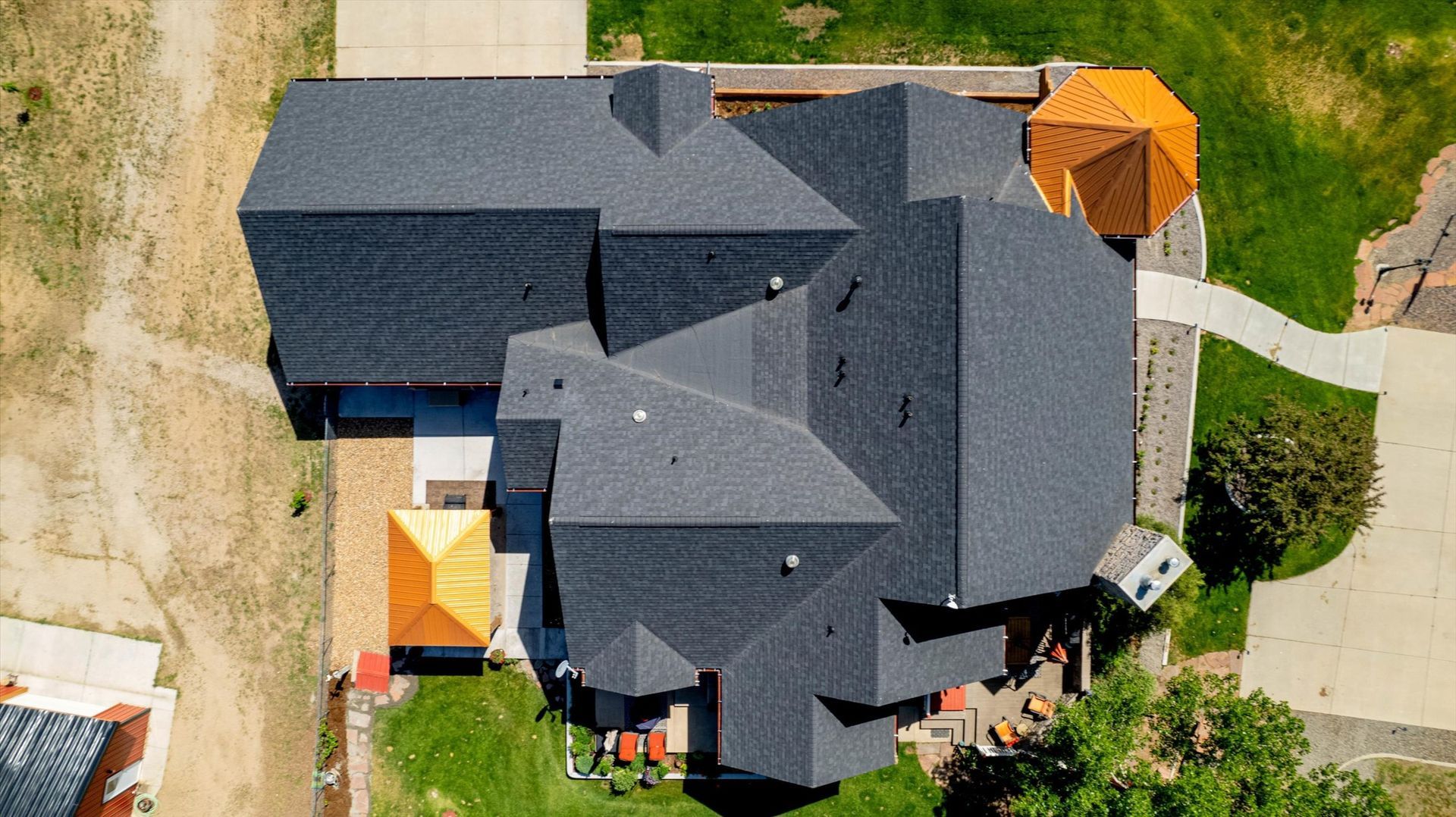 Overhead view of a dark-roofed house with a unique architectural design, surrounded by green grass and a sidewalk.
