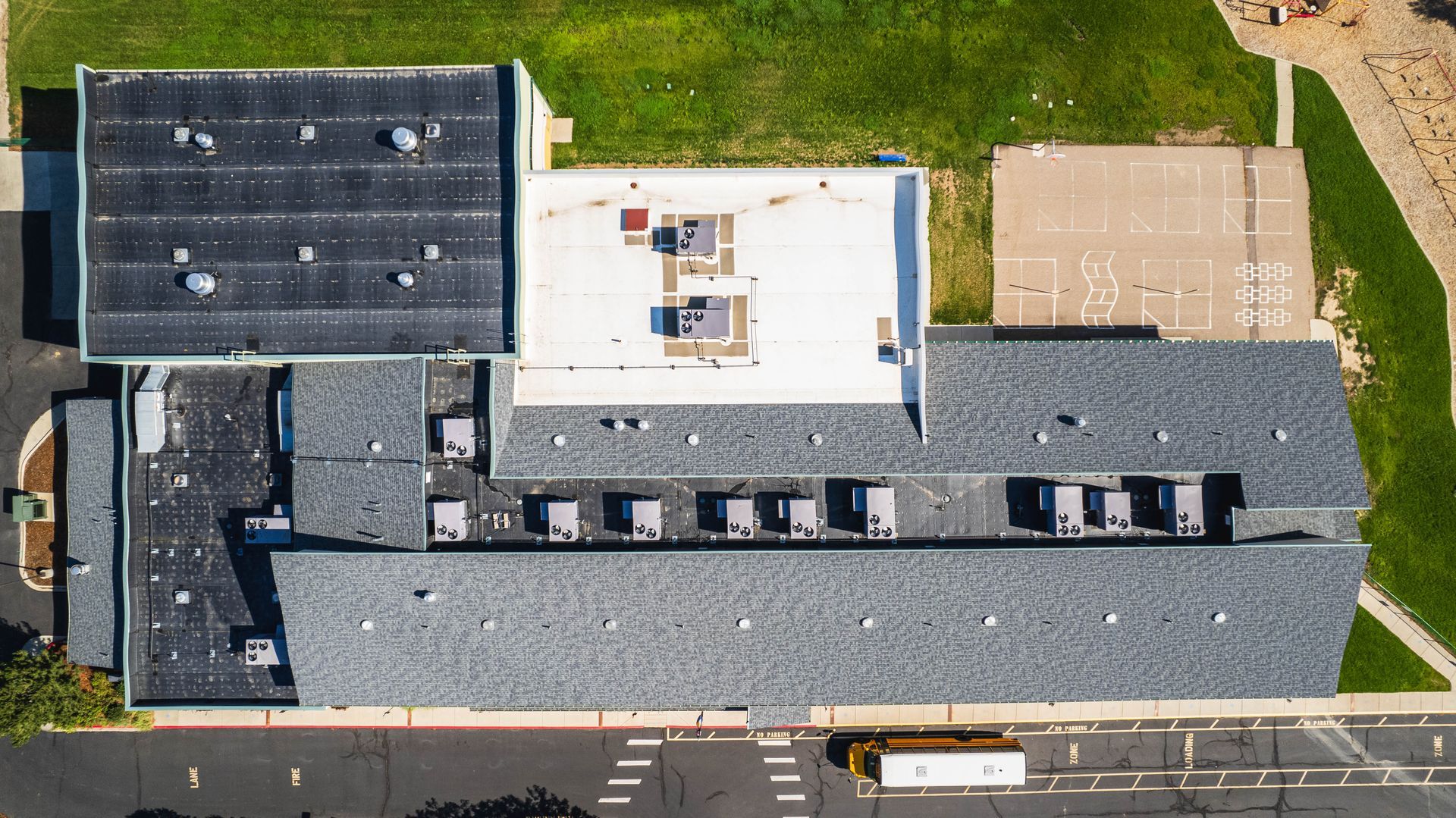 Overhead view of a school building with various roof types and a yellow school bus parked nearby.