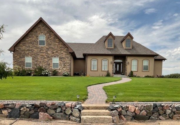 House with stone facade and brown roof, landscaped lawn and path.