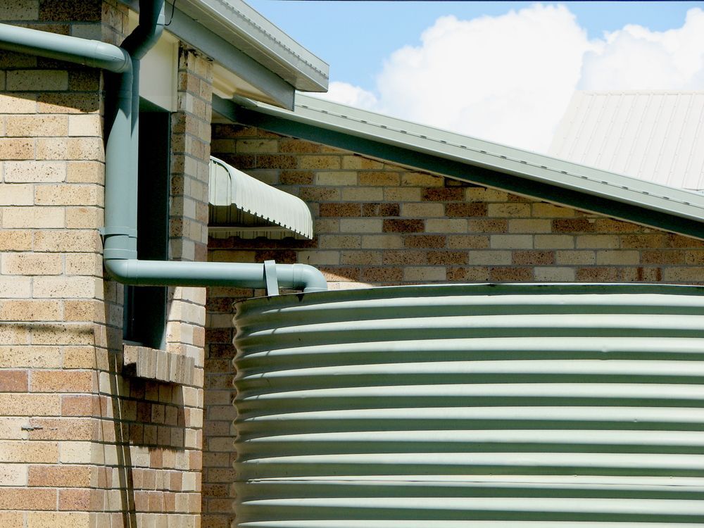 A green water tank is attached to the side of a brick building — Elite Water In Kyogle, NSW