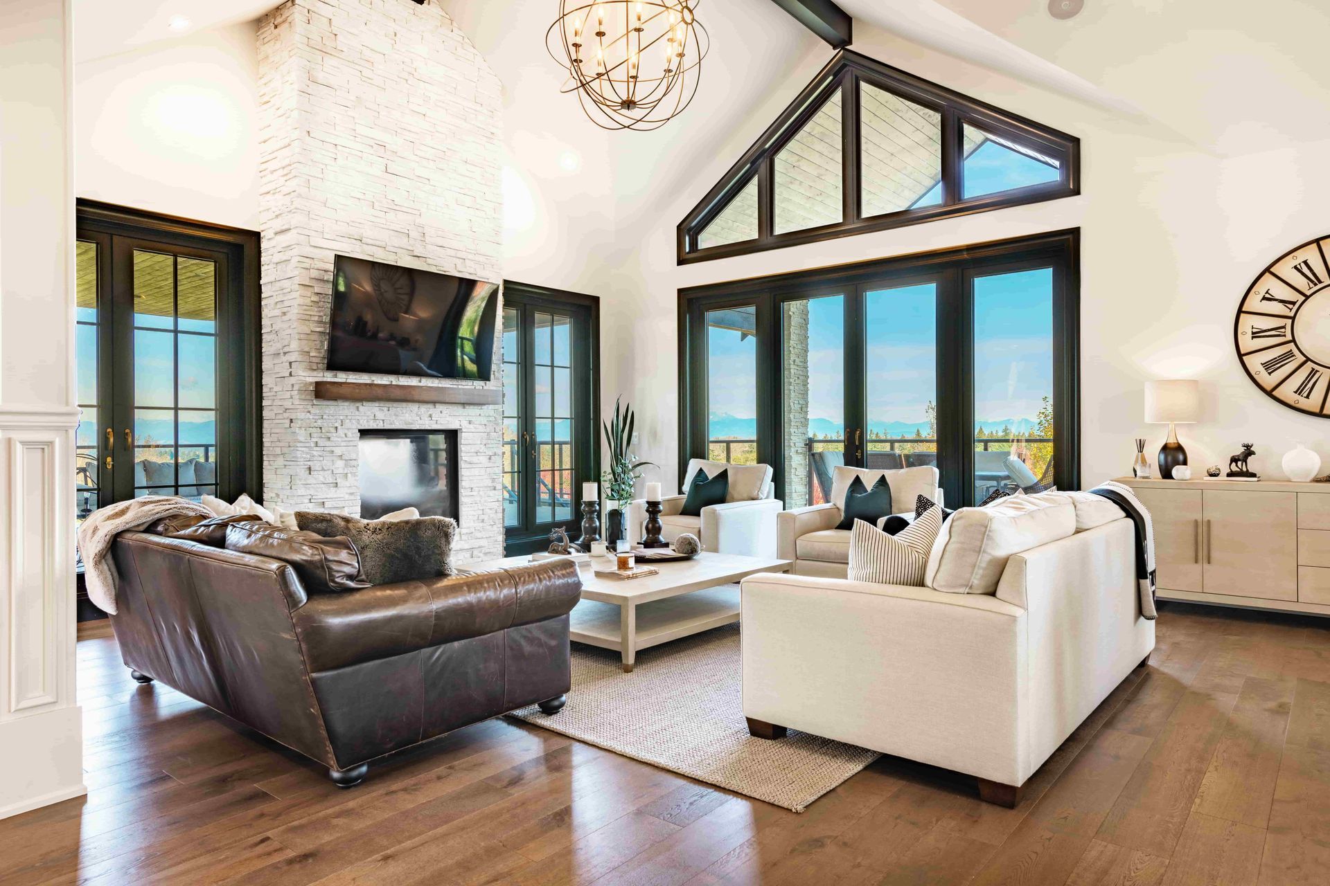Spacious living room with vaulted ceiling, large windows, fireplace, two couches, and white walls.