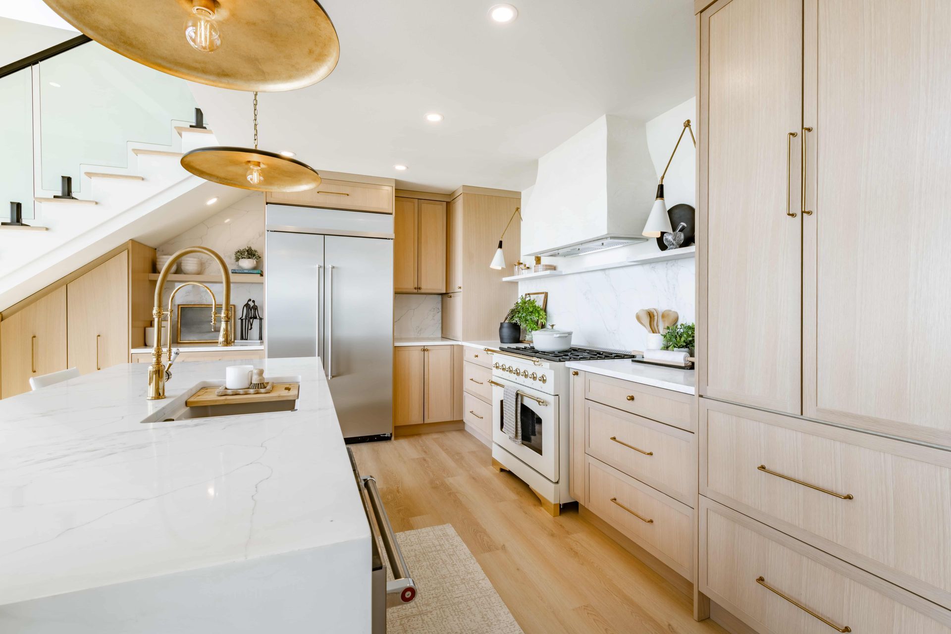 Modern kitchen with light wood cabinets, white countertops, stainless steel appliances, and gold accents.