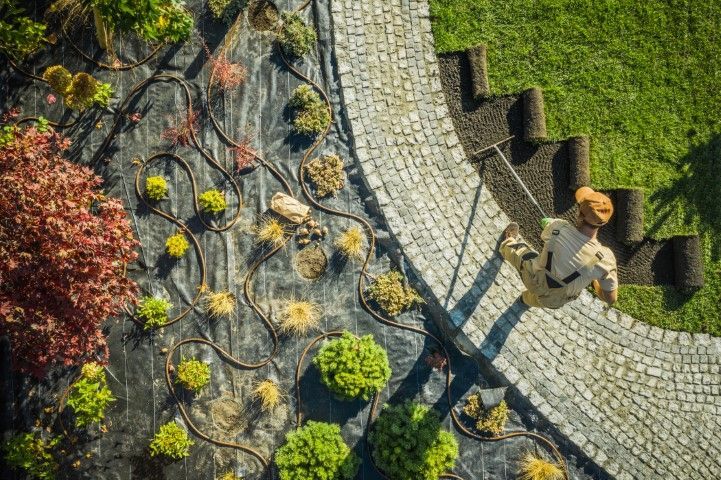 An overhead view of a person laying rolls of grass sod next to a stone path and a landscaped garden bed with mulch.