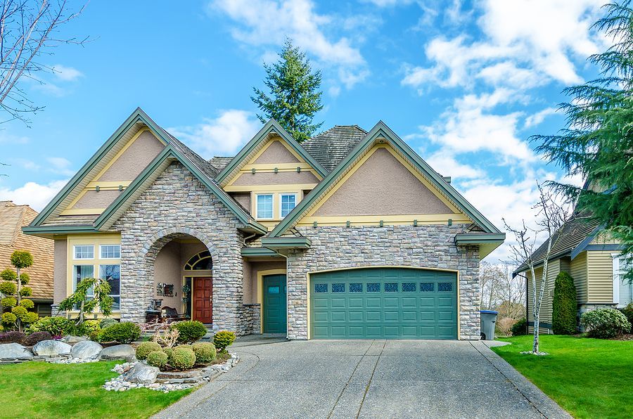 A two-story suburban home with stone veneer siding, a green garage door, a prominent front porch, and a paved driveway.