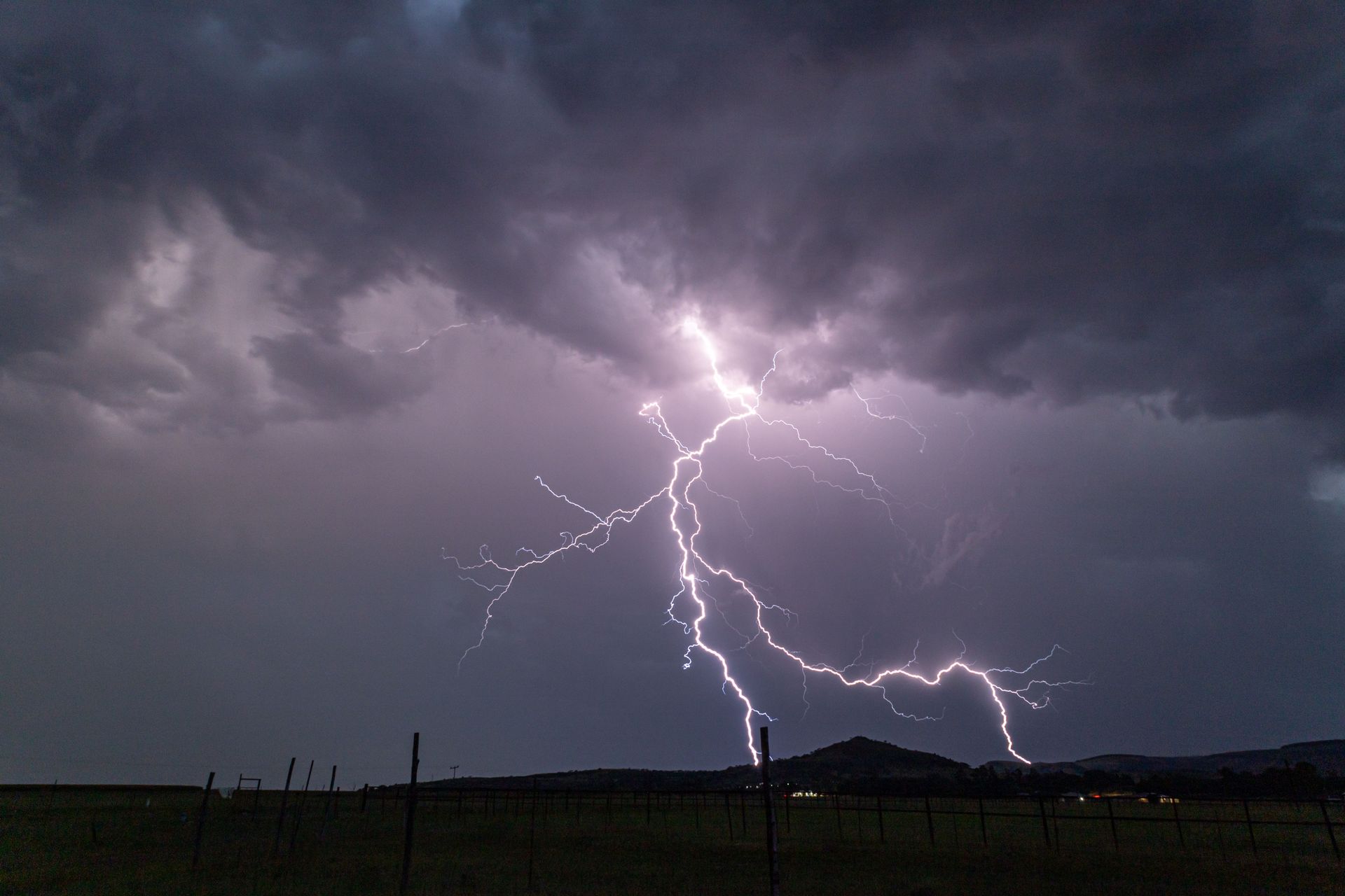 Lightning bolts strike over a dark, stormy field beneath heavy clouds