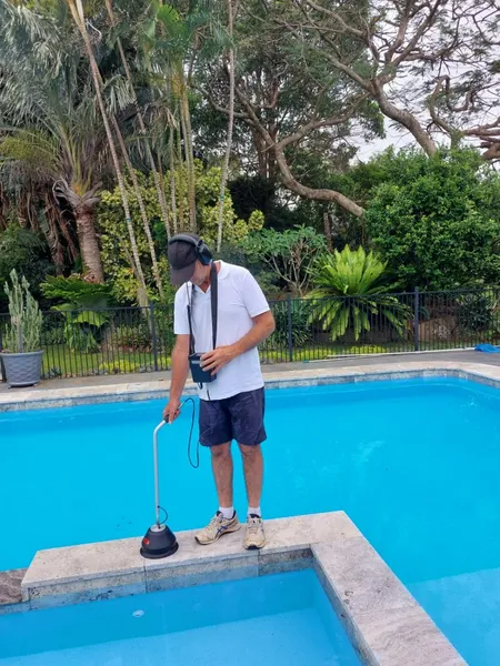 Person using a listening device to check a pool for leaks. Outdoors with trees and fence.