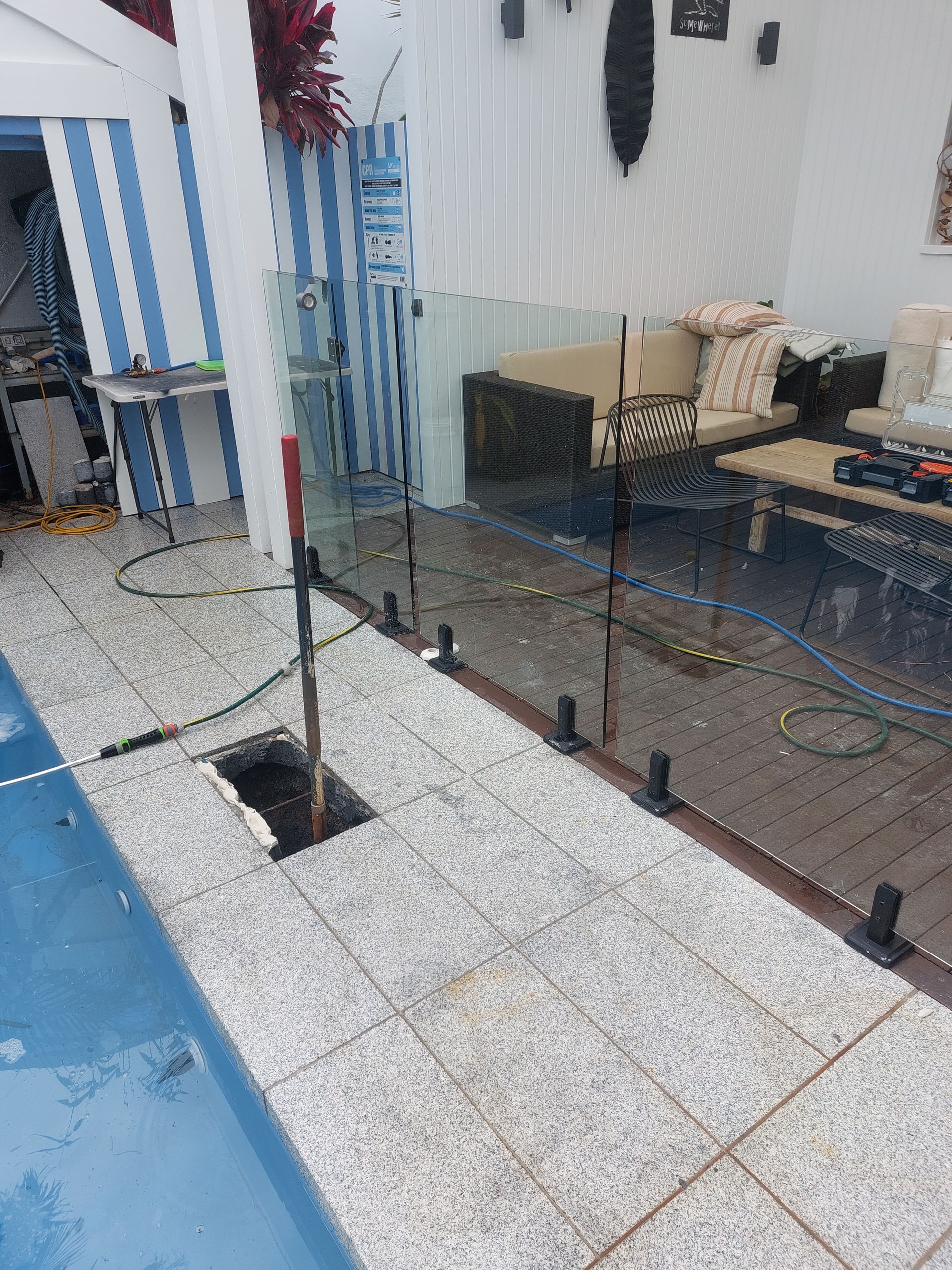 Glass pool fence installation in progress, near blue pool and tiled deck.