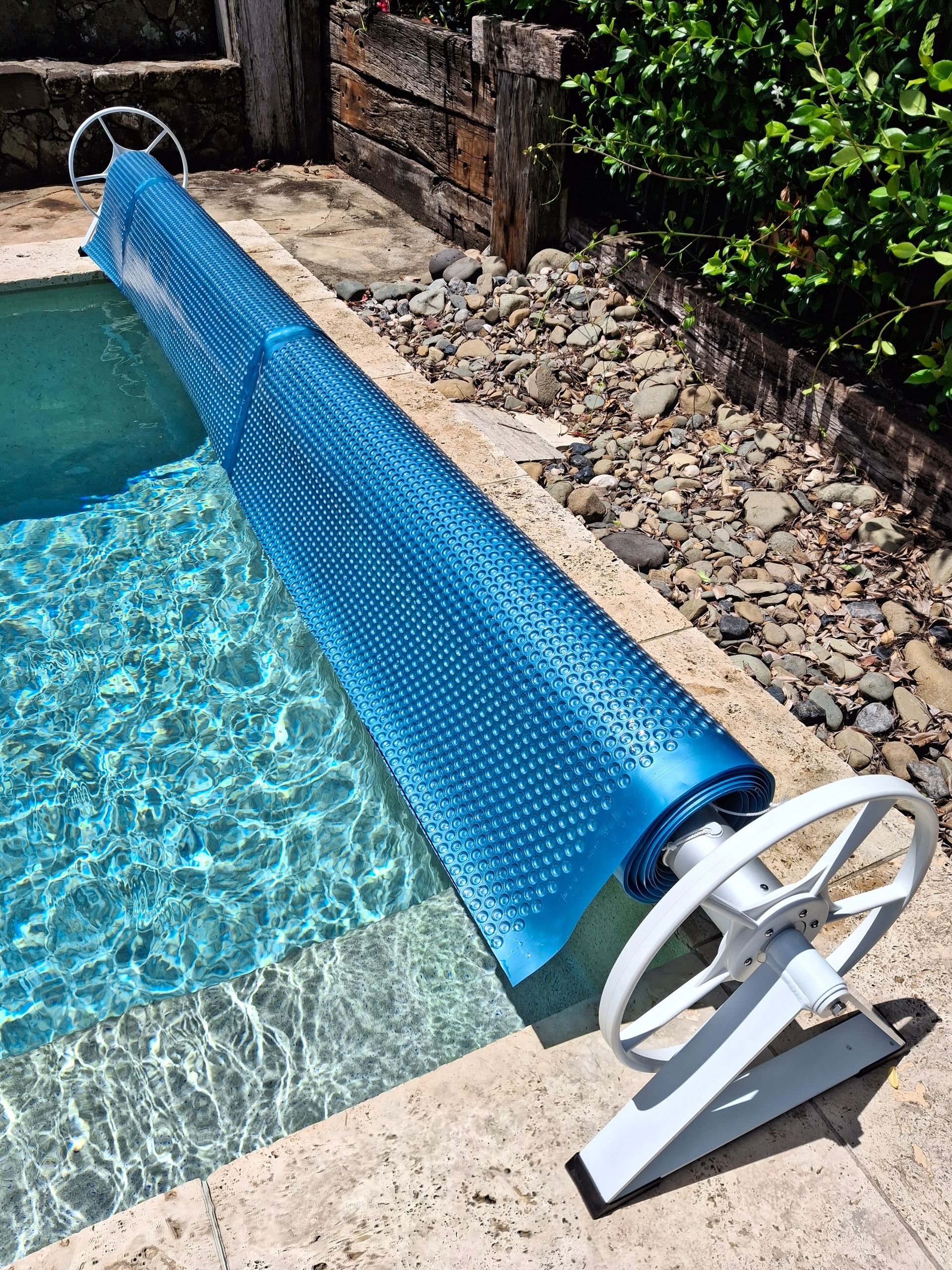 Blue bubble pool cover rolled up on white reel, beside a pool.