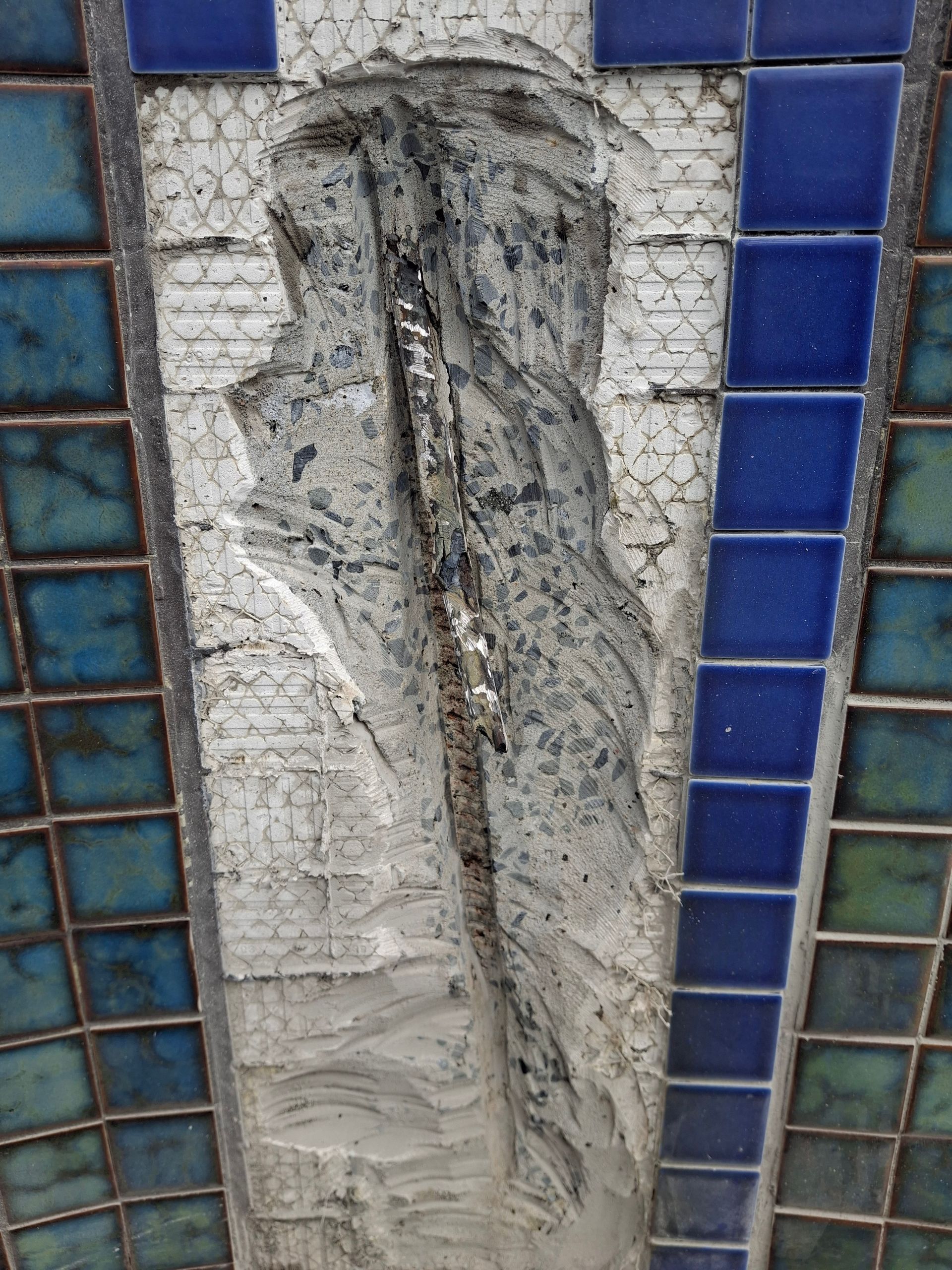 Stone relief of two figures, textured, within blue and teal tiled architectural elements.