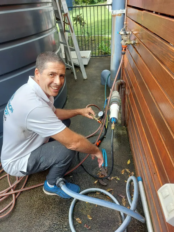 Man Crouched Near a Building, Working on Plumbing With Hoses and Equipment — Ballina Leak Detection & Swimming Pool Repairs in Ballina, NSW