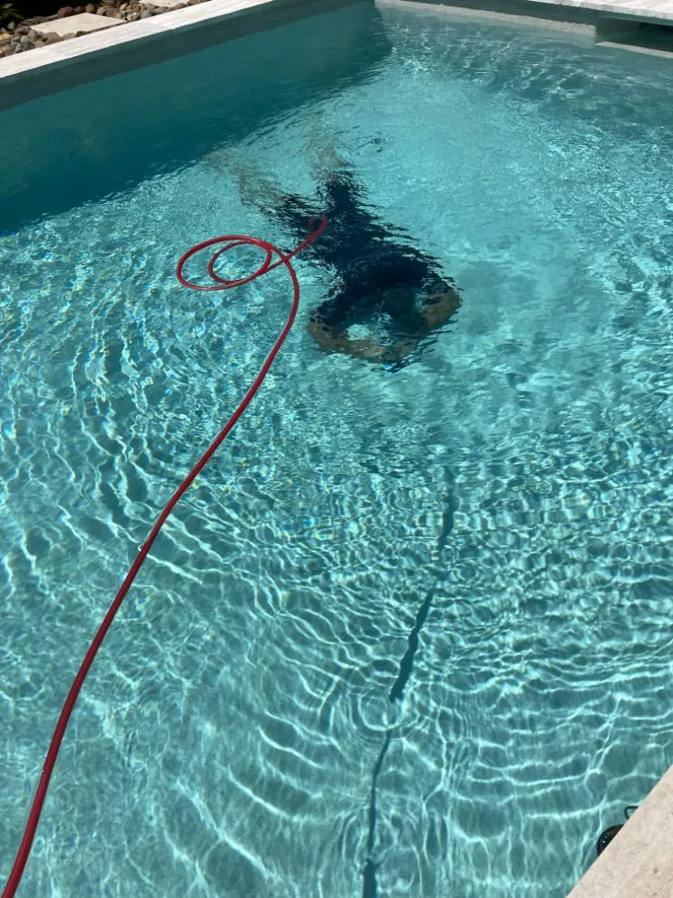 Person Cleaning a Swimming Pool With a Red Hose Underwater — Ballina Leak Detection & Swimming Pool Repairs in Ballina, NSW