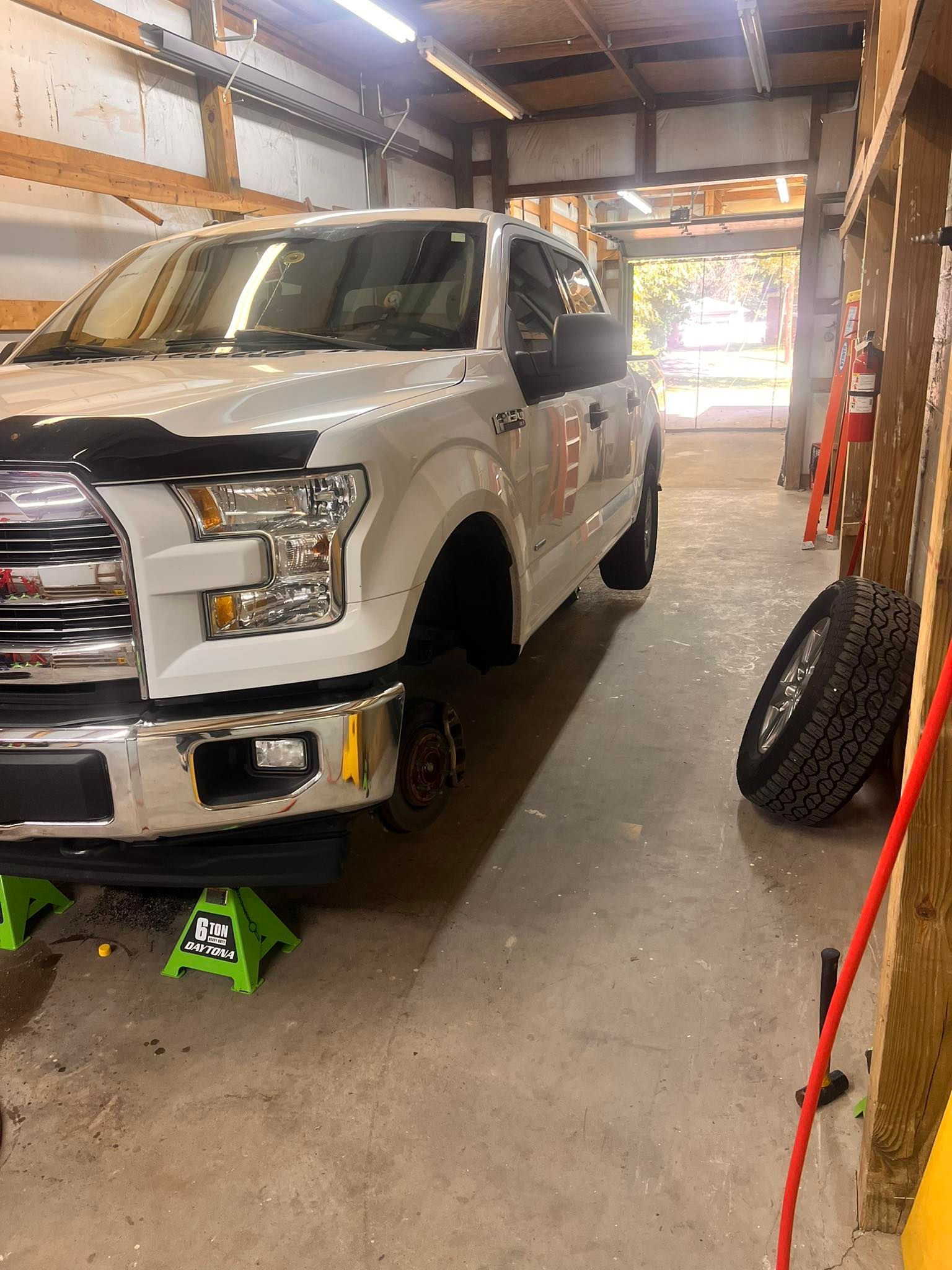 White pickup truck on jack stands in a garage; spare tire leaning against a wall.