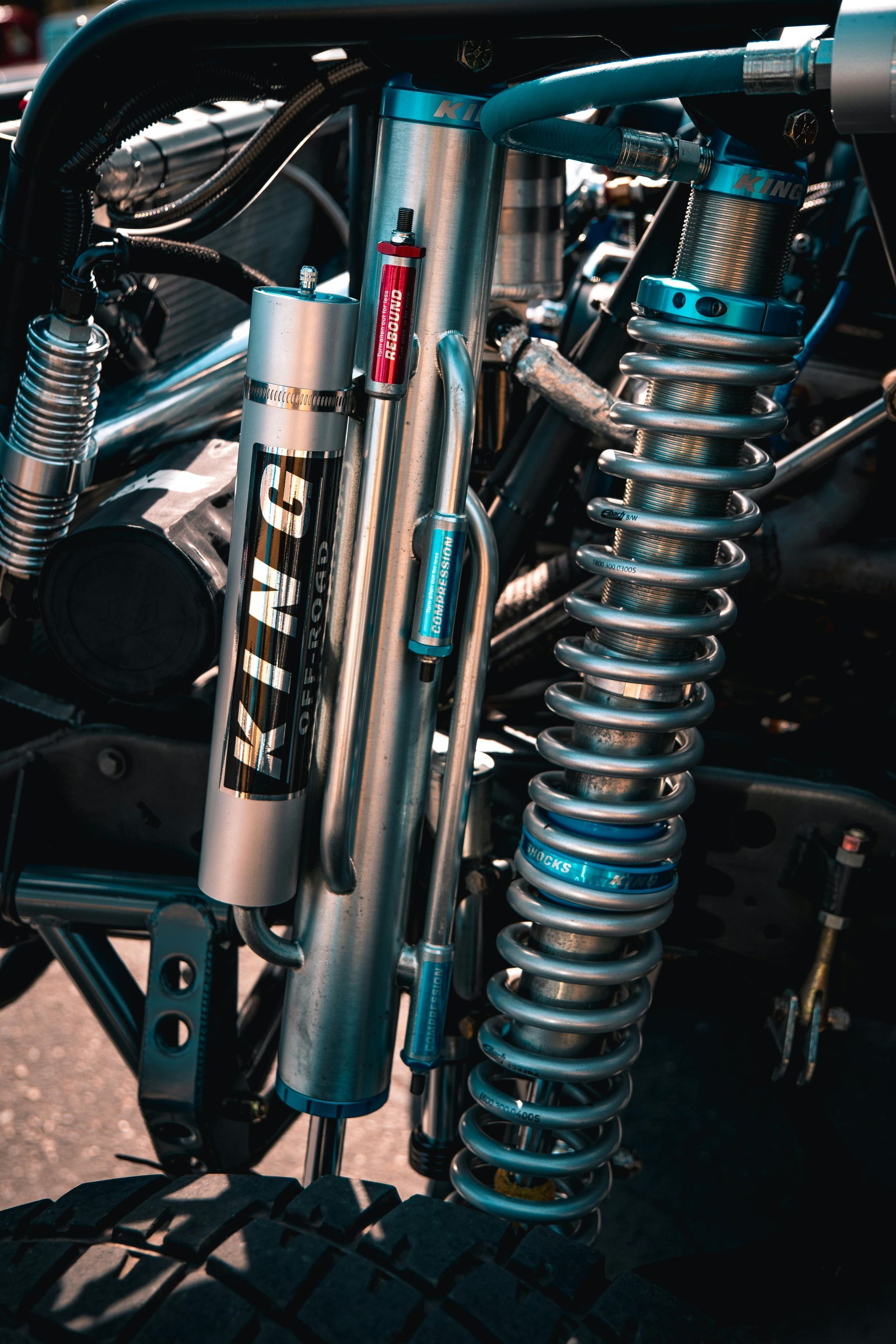 Close-up of a truck's suspension system. King shocks, coil-over springs, and hydraulic tubing are visible.