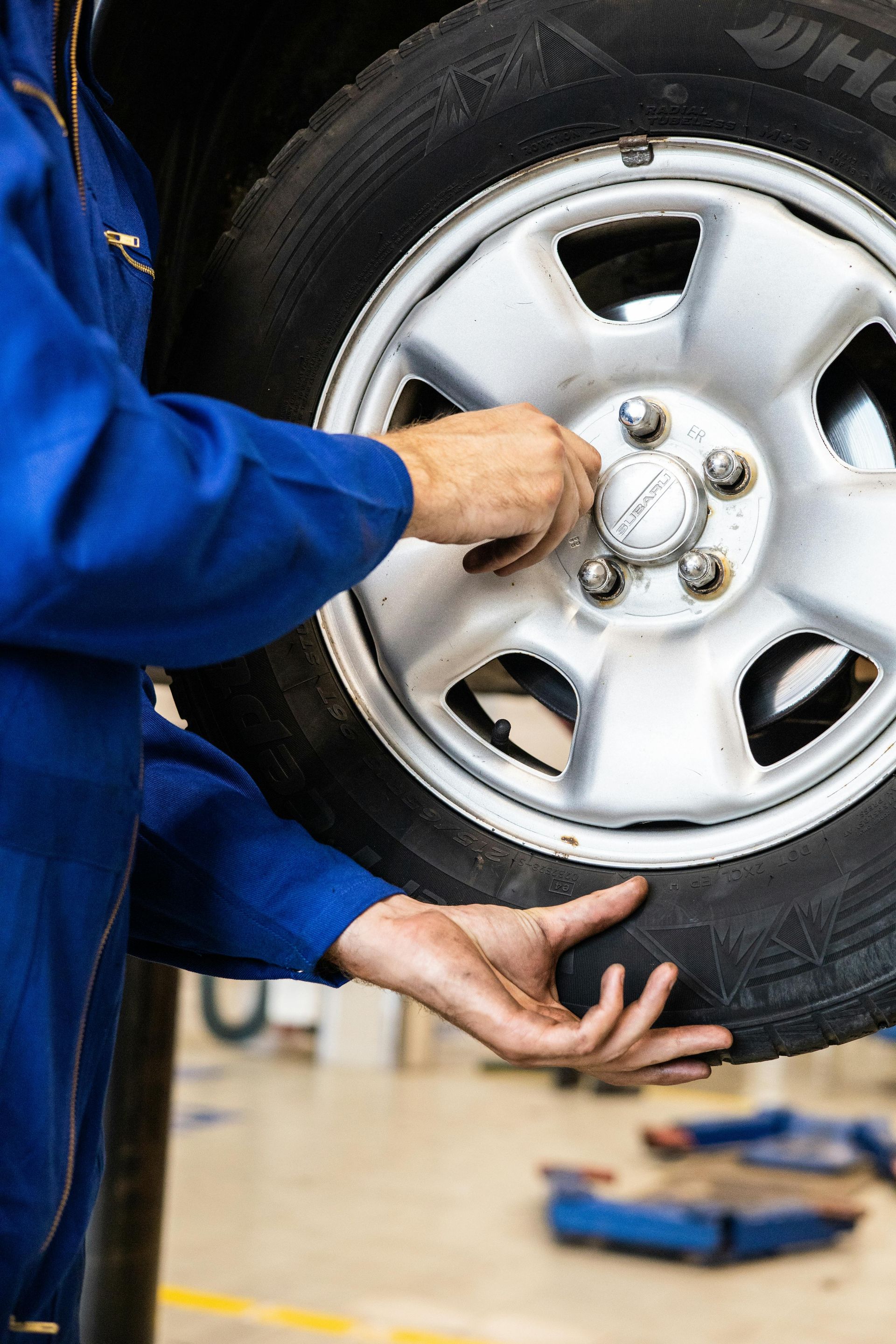 Mechanic in blue jumpsuit removes wheel from a car in a workshop.