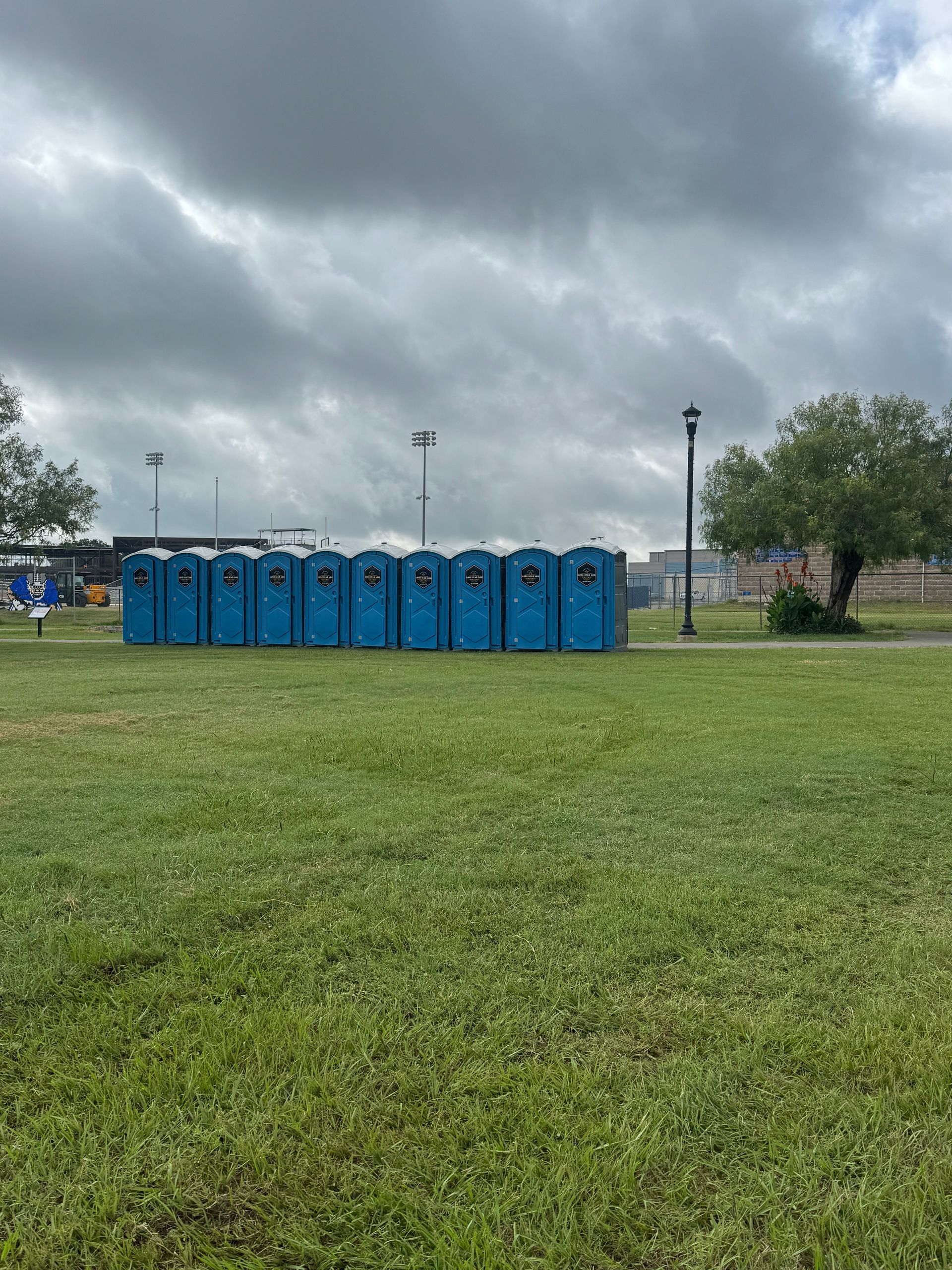 Blue portable toilets on a grassy field under dark storm clouds.