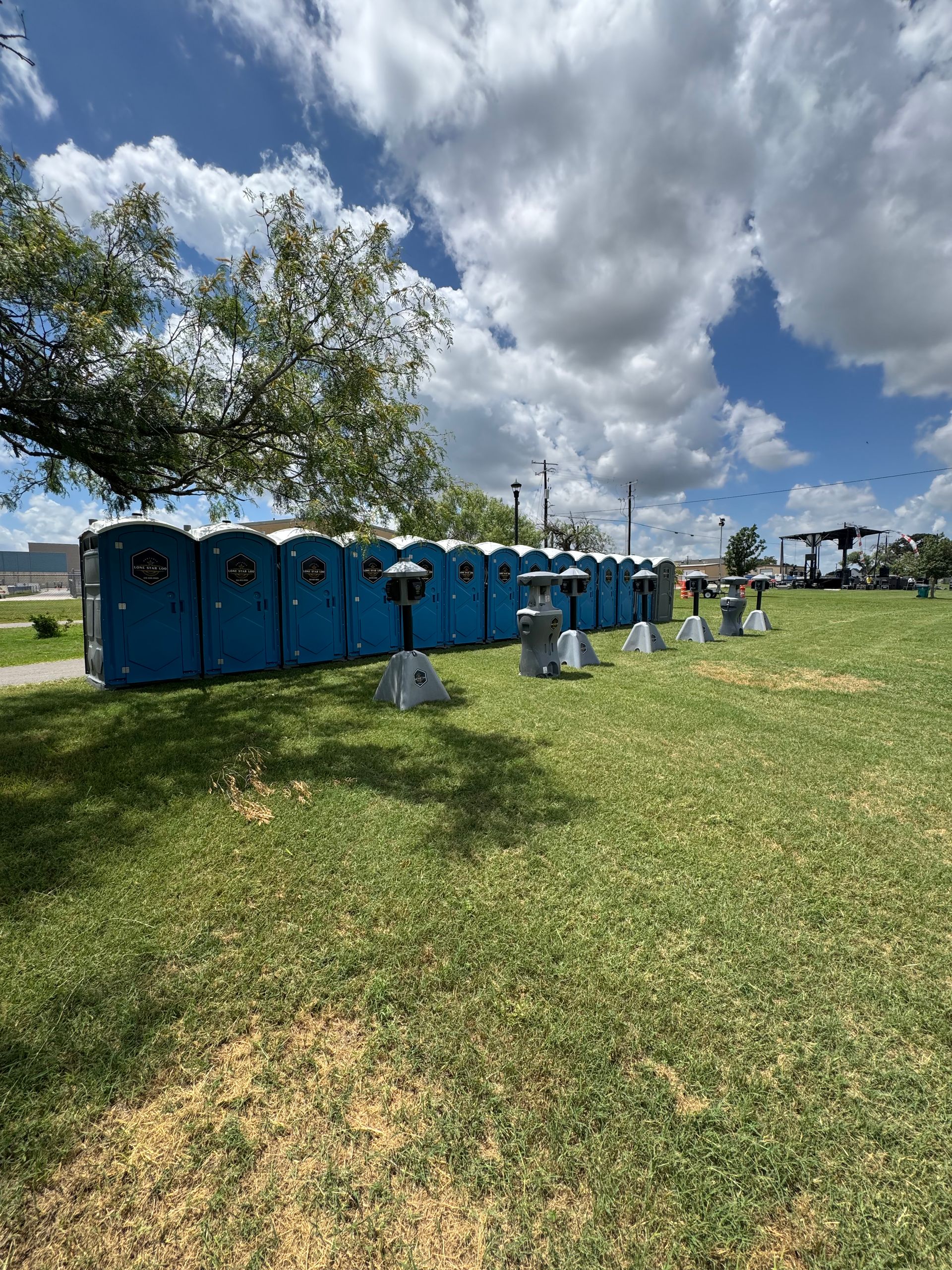 Blue portable toilets lined up on a grassy field under a cloudy sky.
