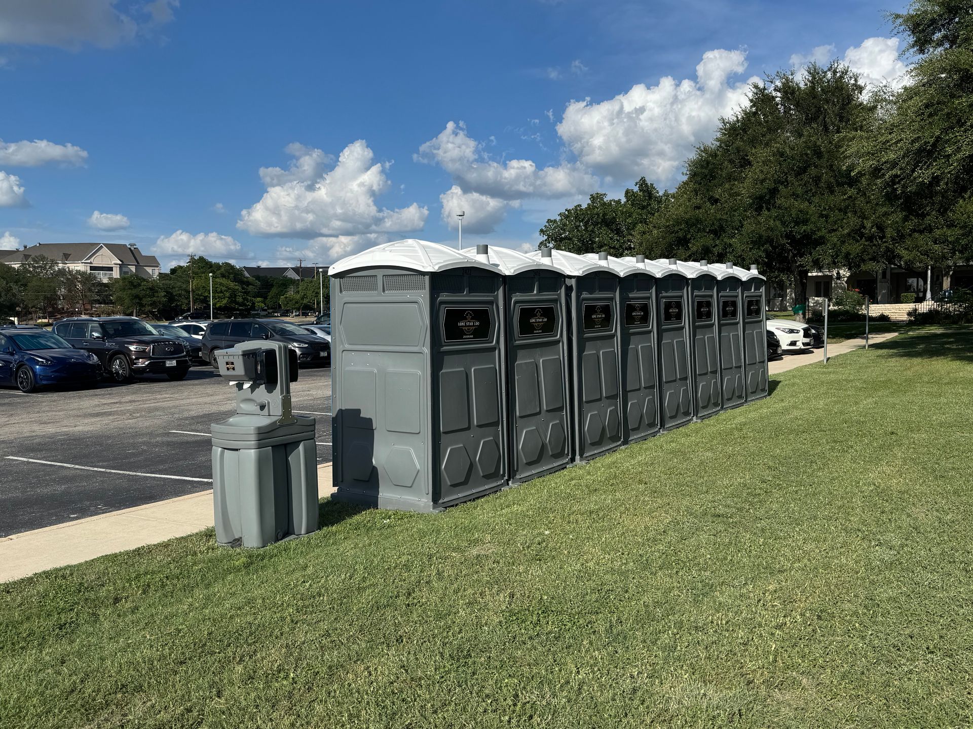 Four yellow portable toilets lined up on a dirt field under a cloudy sky.