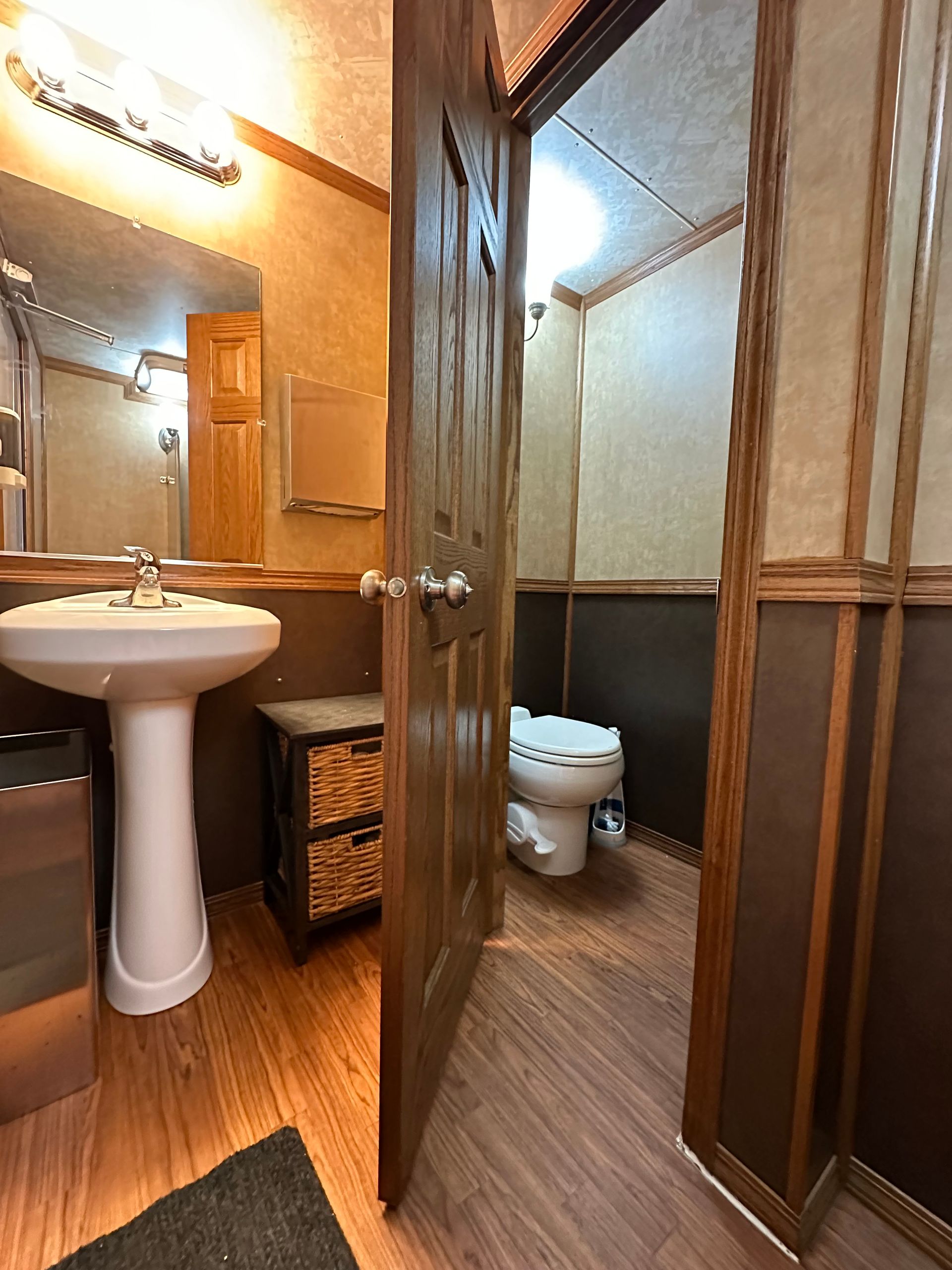 Compact bathroom with pedestal sink, toilet, glass shower, and wood-paneled walls and floor.
