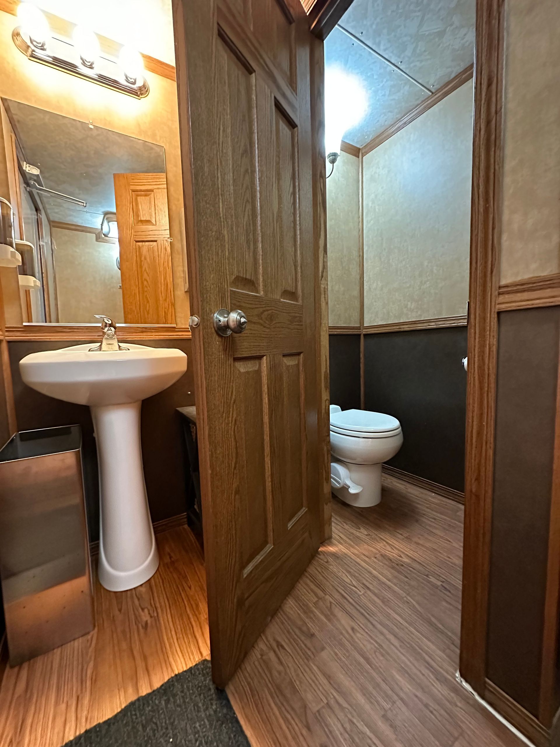 Small bathroom with pedestal sink, open wooden door, toilet, and wood-paneled walls