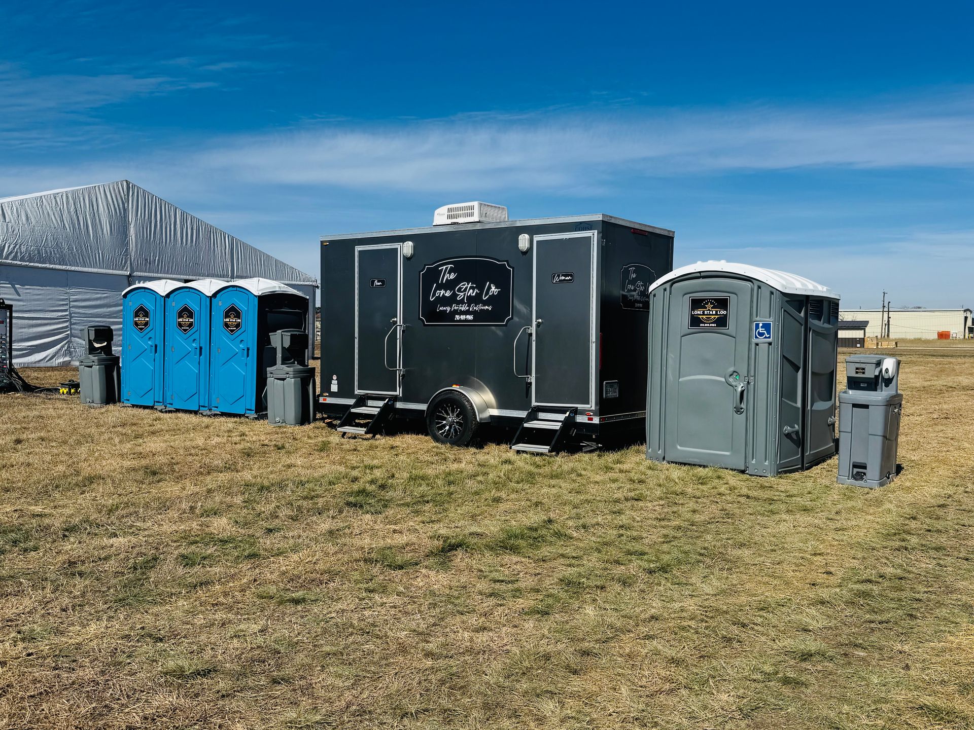 Portable toilets lined up on a grassy field under a blue sky, with a mountain in the background