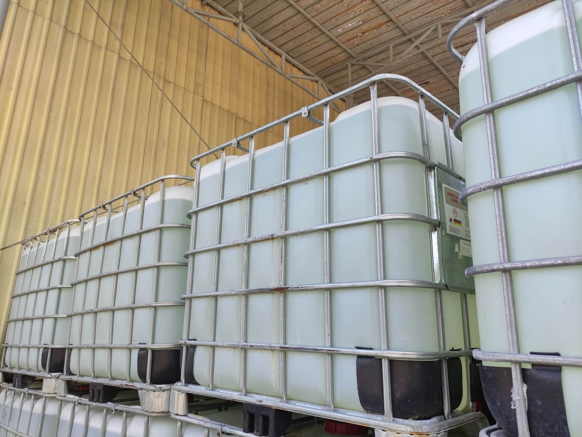 White industrial storage tanks with metal cages lined up inside a warehouse under a curved ceiling
