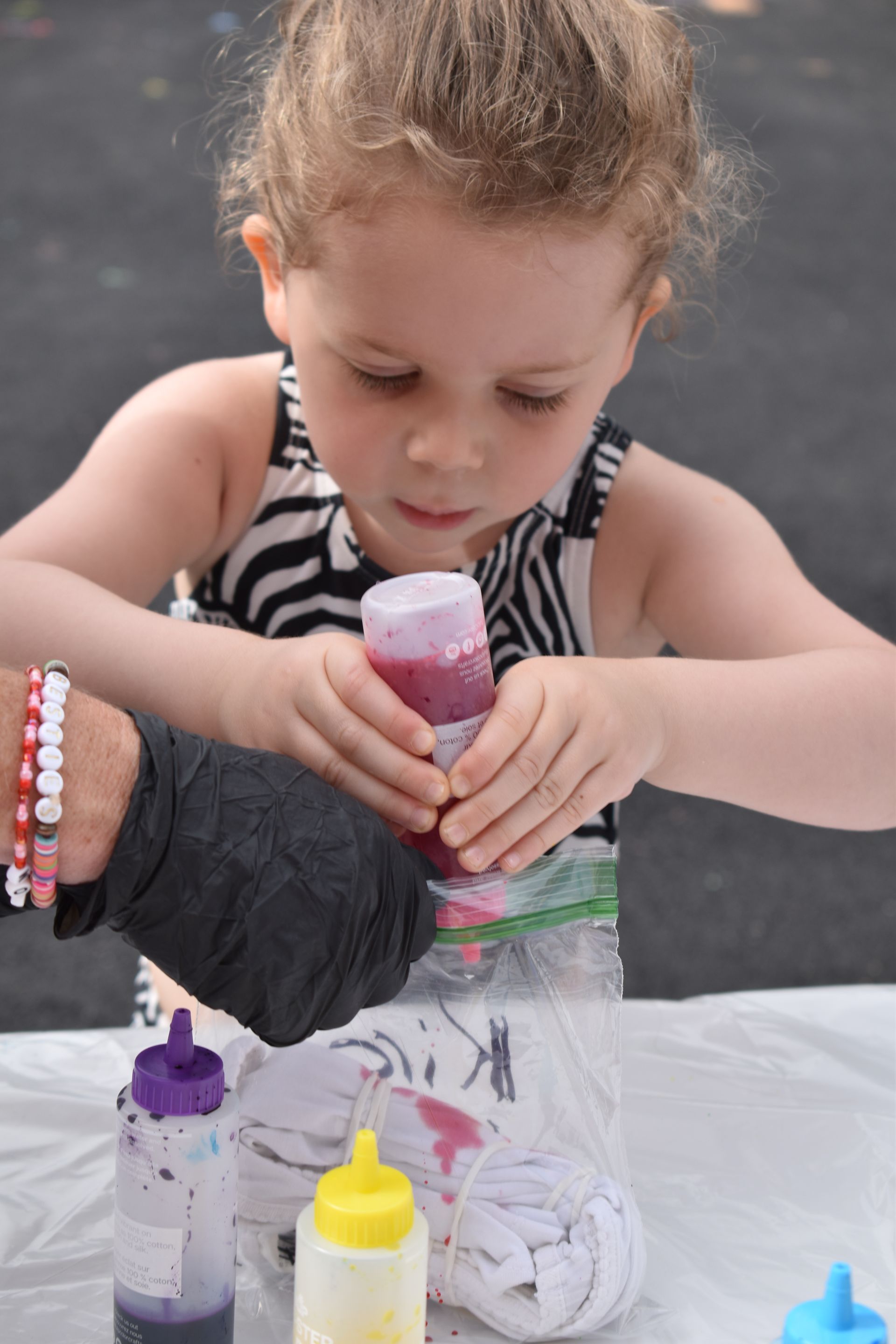 A little girl in a zebra print tank top is playing with bottles of paint