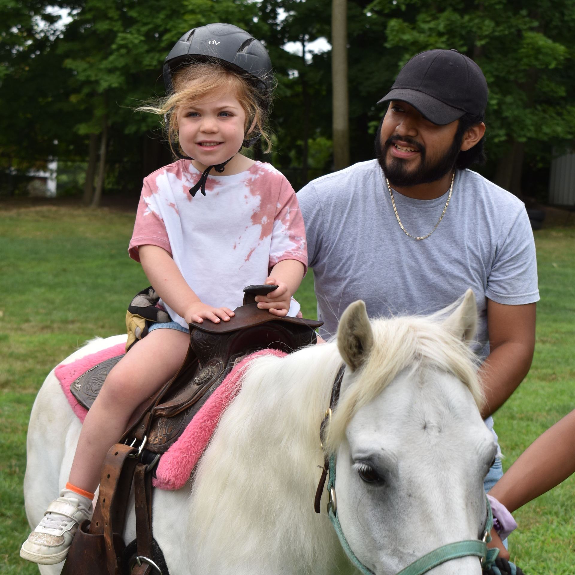 A little girl wearing a helmet is riding a white pony