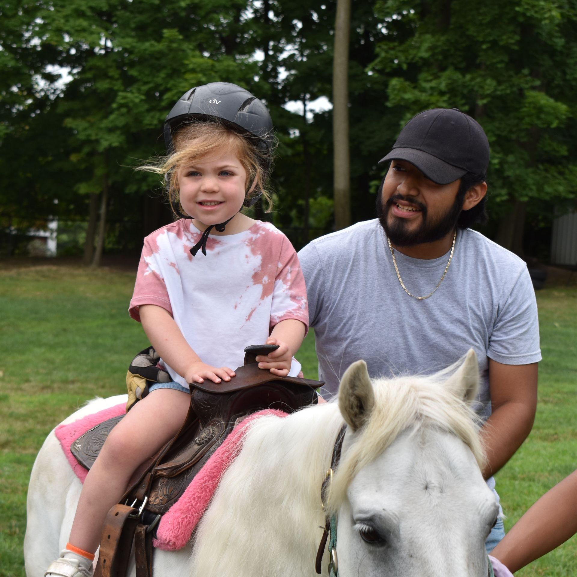 A little girl wearing a helmet is riding a white horse