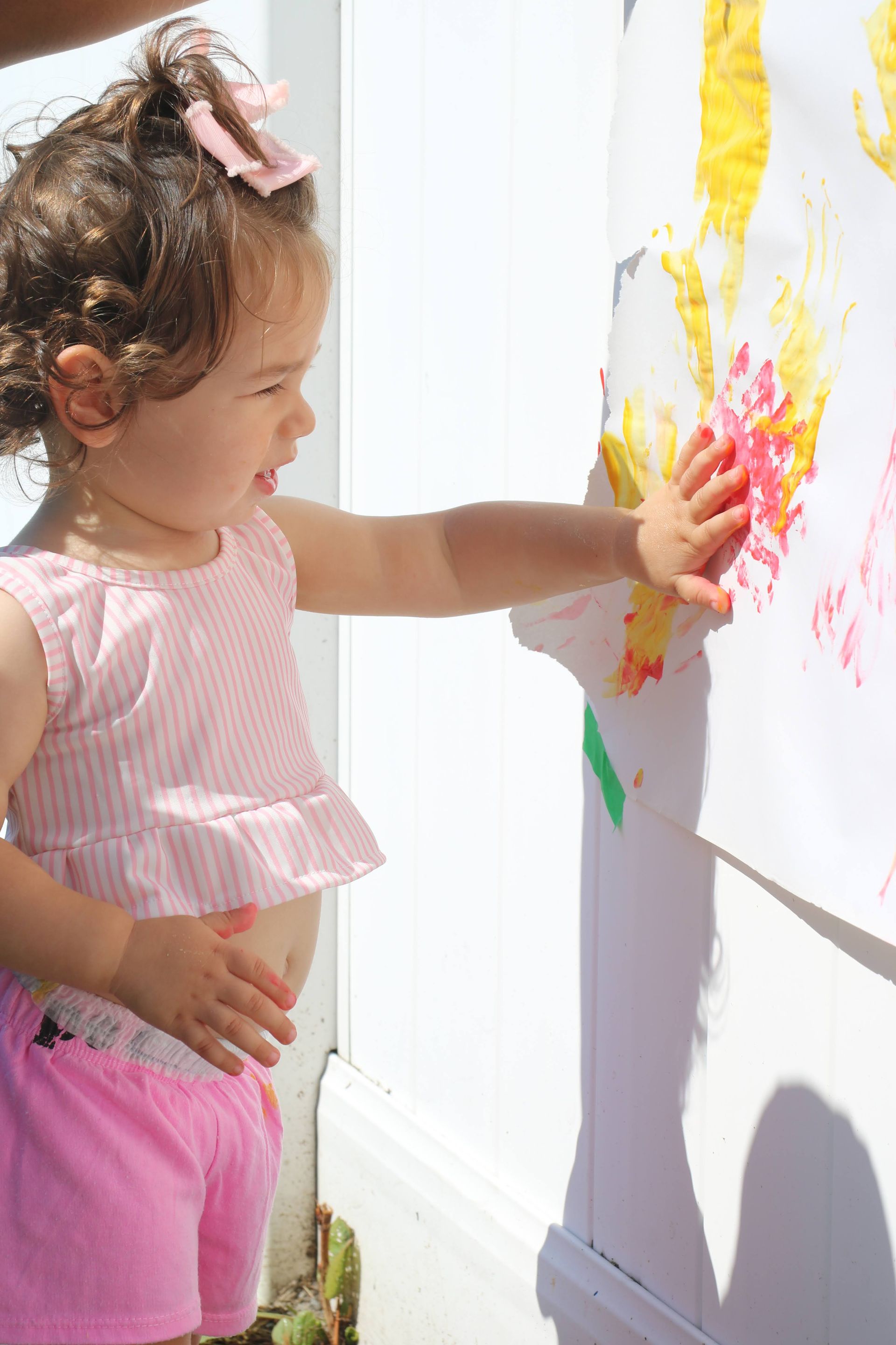 A little girl is painting on a wall with her hands.