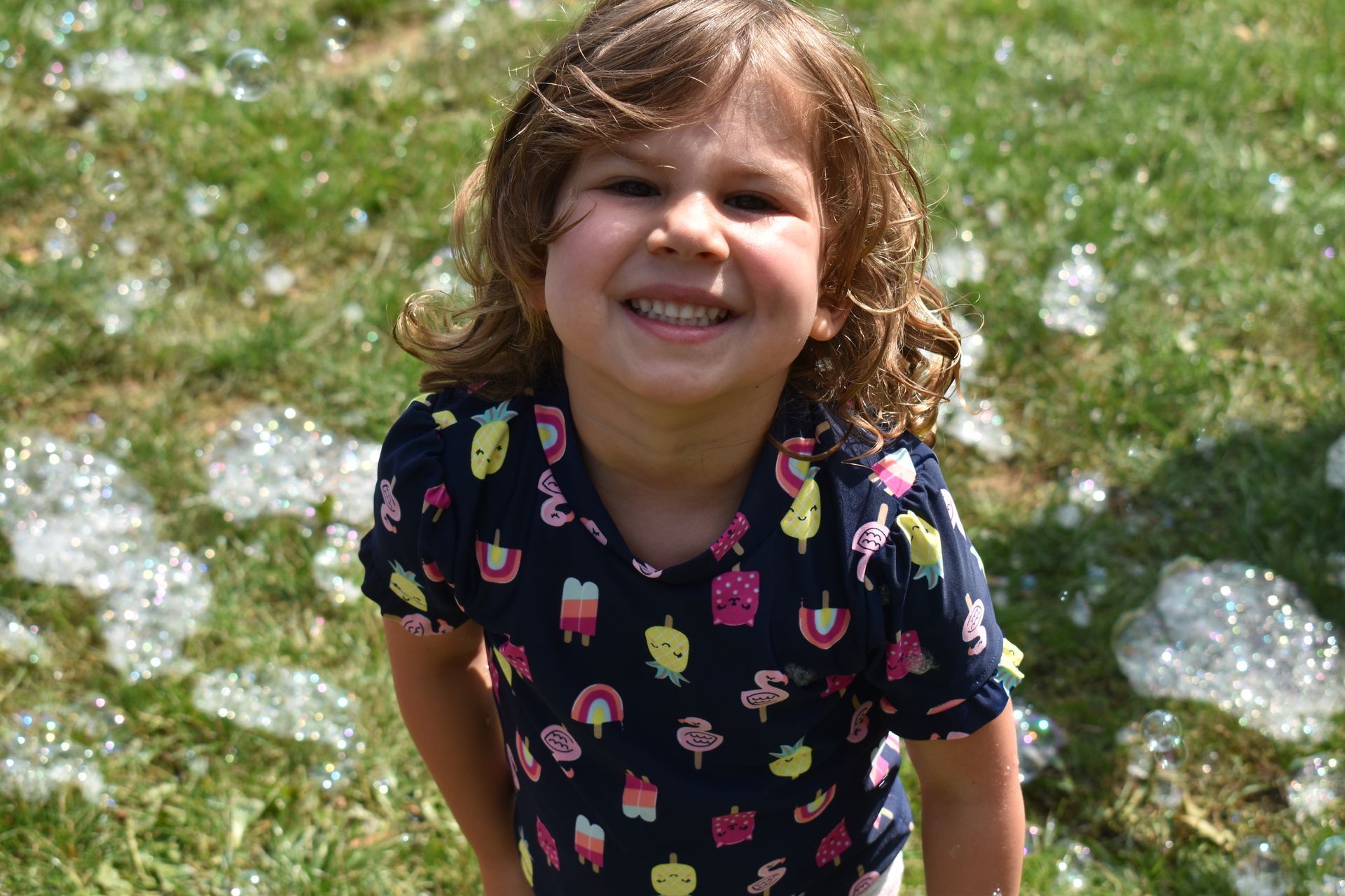 A little boy is standing in the grass surrounded by soap bubbles.