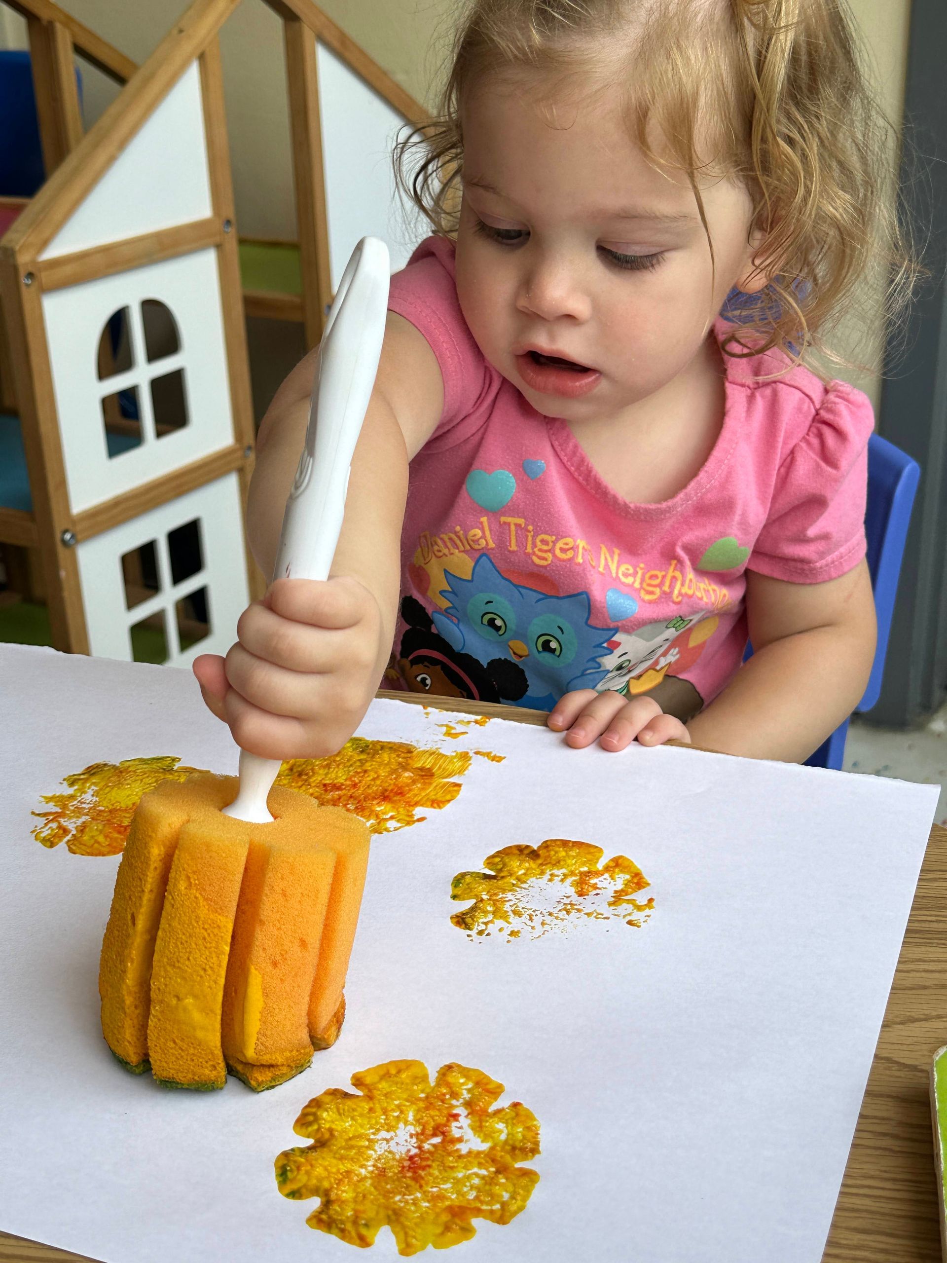 A little girl in a pink shirt is painting with a sponge