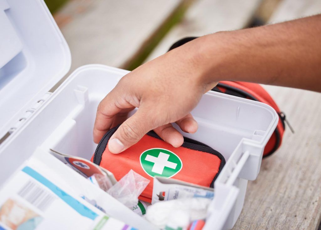 Hand reaching into a white first aid kit, pulling out a small red medical pouch.