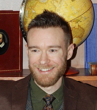 A man in a suit and tie smiles in front of a globe