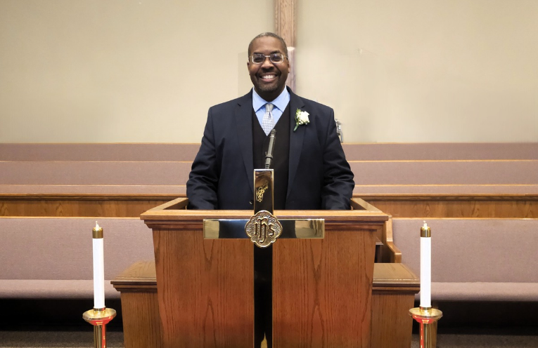 Man in suit smiles at lectern in church.