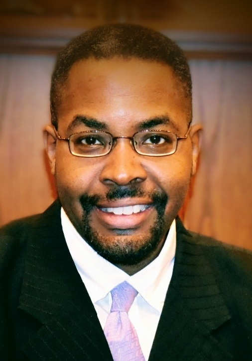 Man with glasses, smiling, wearing a suit and tie.