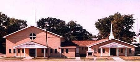 Brick church buildings with a steeple and trees in the background.
