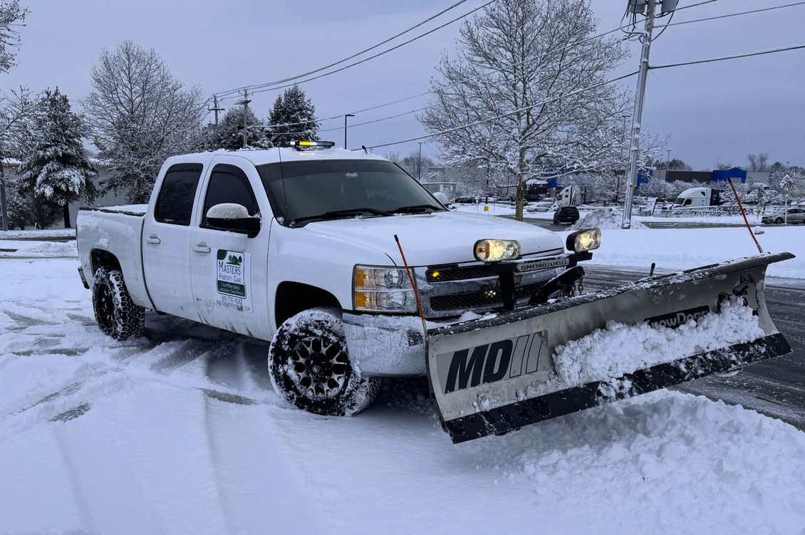 White pickup truck with front plow clearing snow on a snowy road under cloudy winter skies