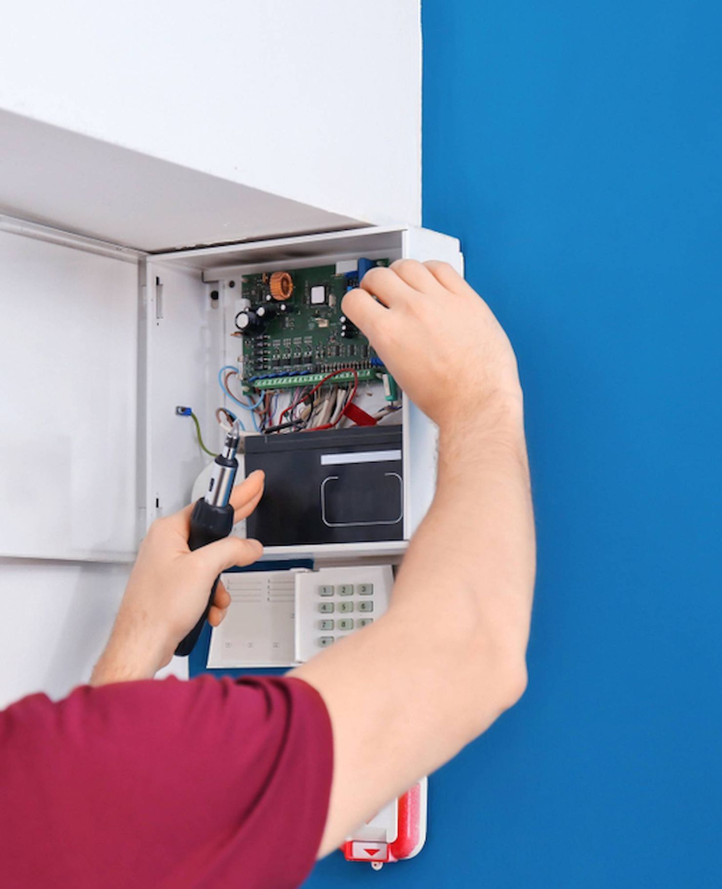 A Man is Installing a Security System on a Blue Wall — Adept Security In Wollongong, NSW