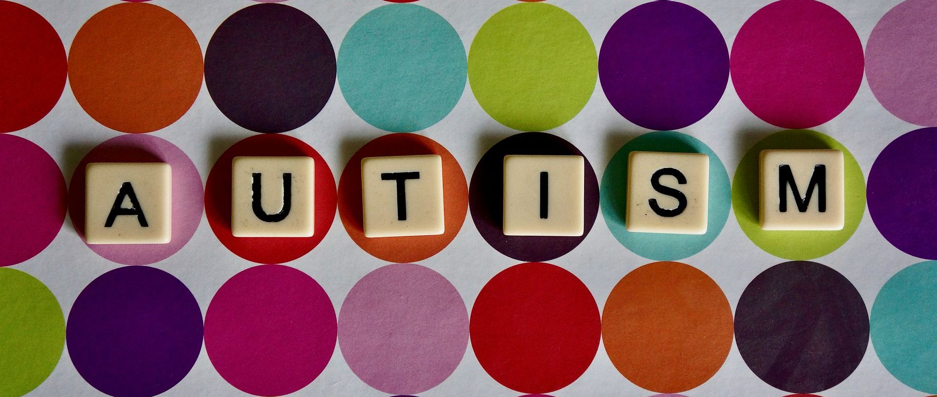 The word autism is written on a colorful polka dot background